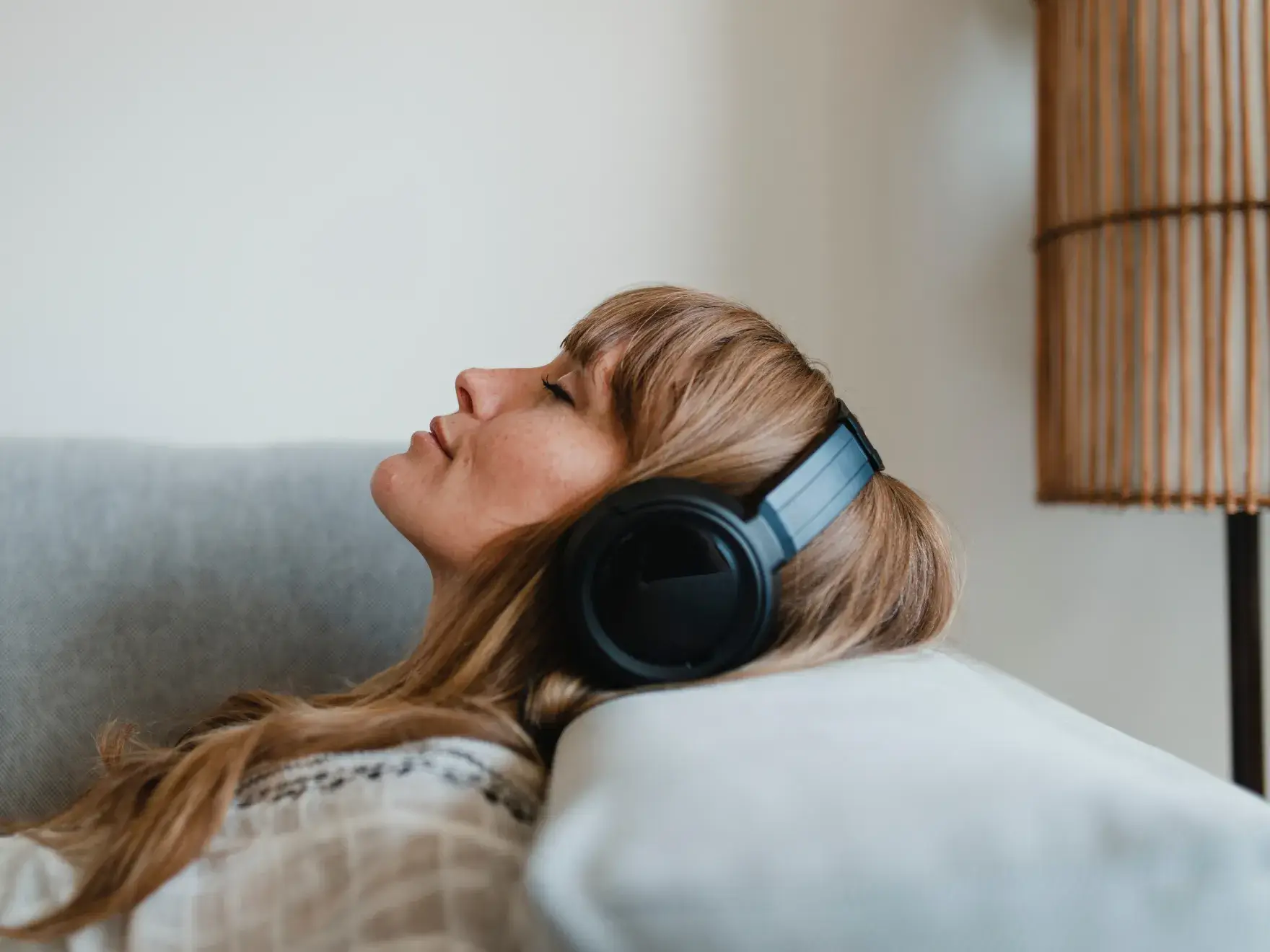 A woman wearing headphones leans back on a couch, eyes closed and relaxed.