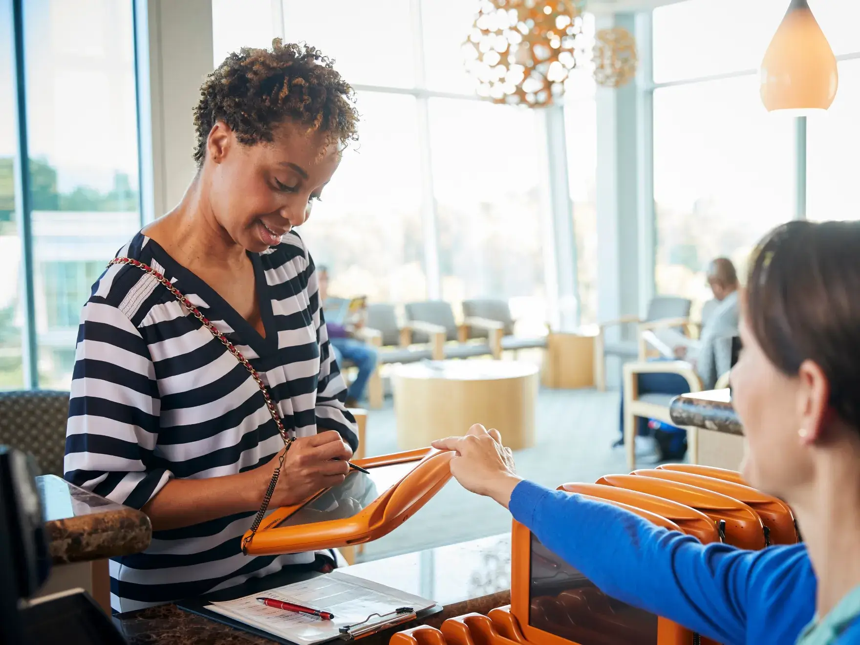 A woman checks in at a hotel front desk, signing paperwork held by a receptionist.