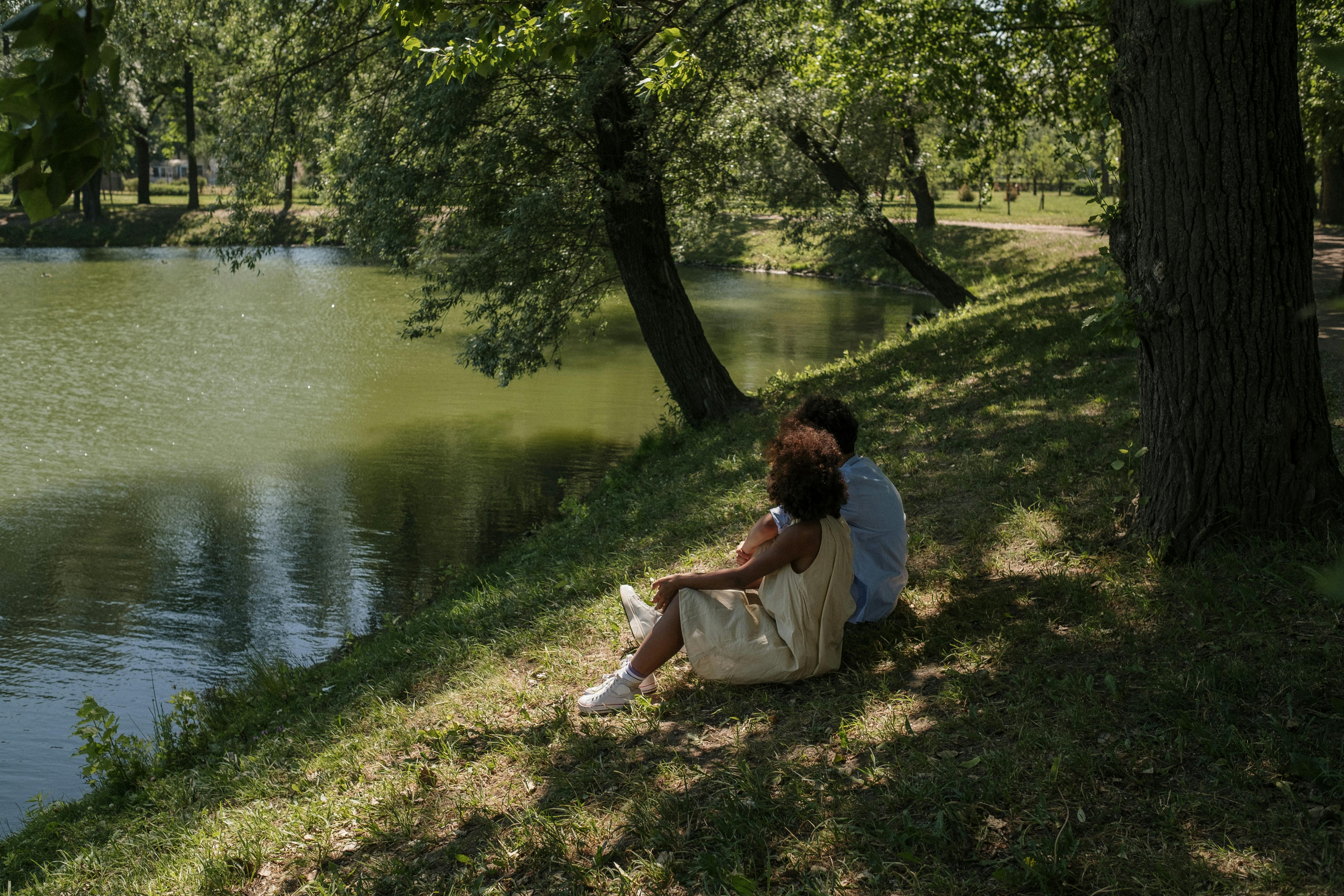 A couple sitting on the grass by the river.