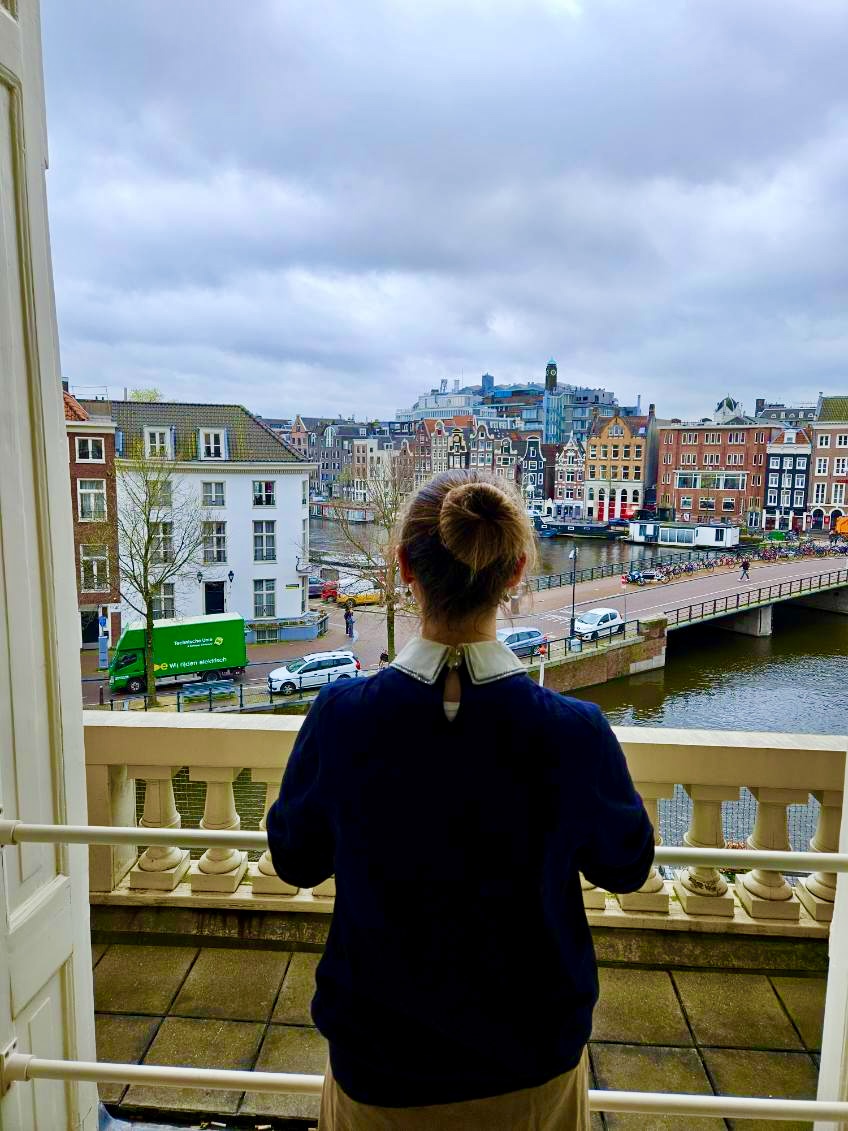 Mari-Alina Timoshchuk looking upon the city of Amsterdam with its colorful houses and canals. She is wearing a blue sweater and her hair is in a bun. 