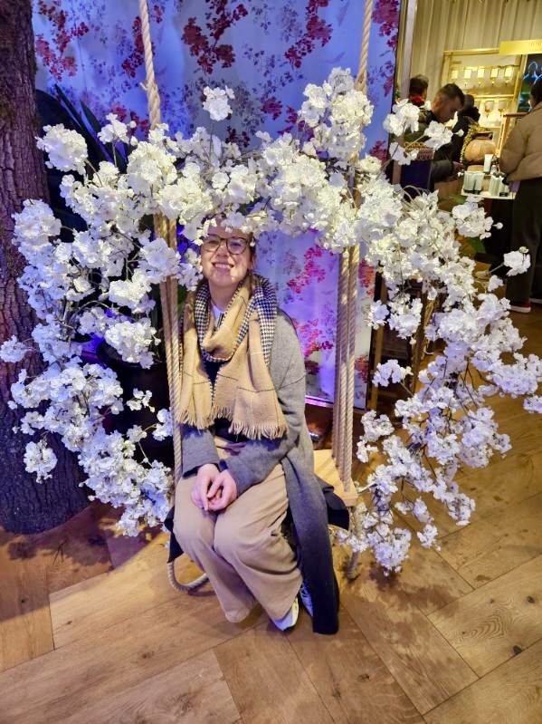 Mari-Alina Timoshchuk sitting on a swing surrounded by white flowers in a store in Amsterdam. 