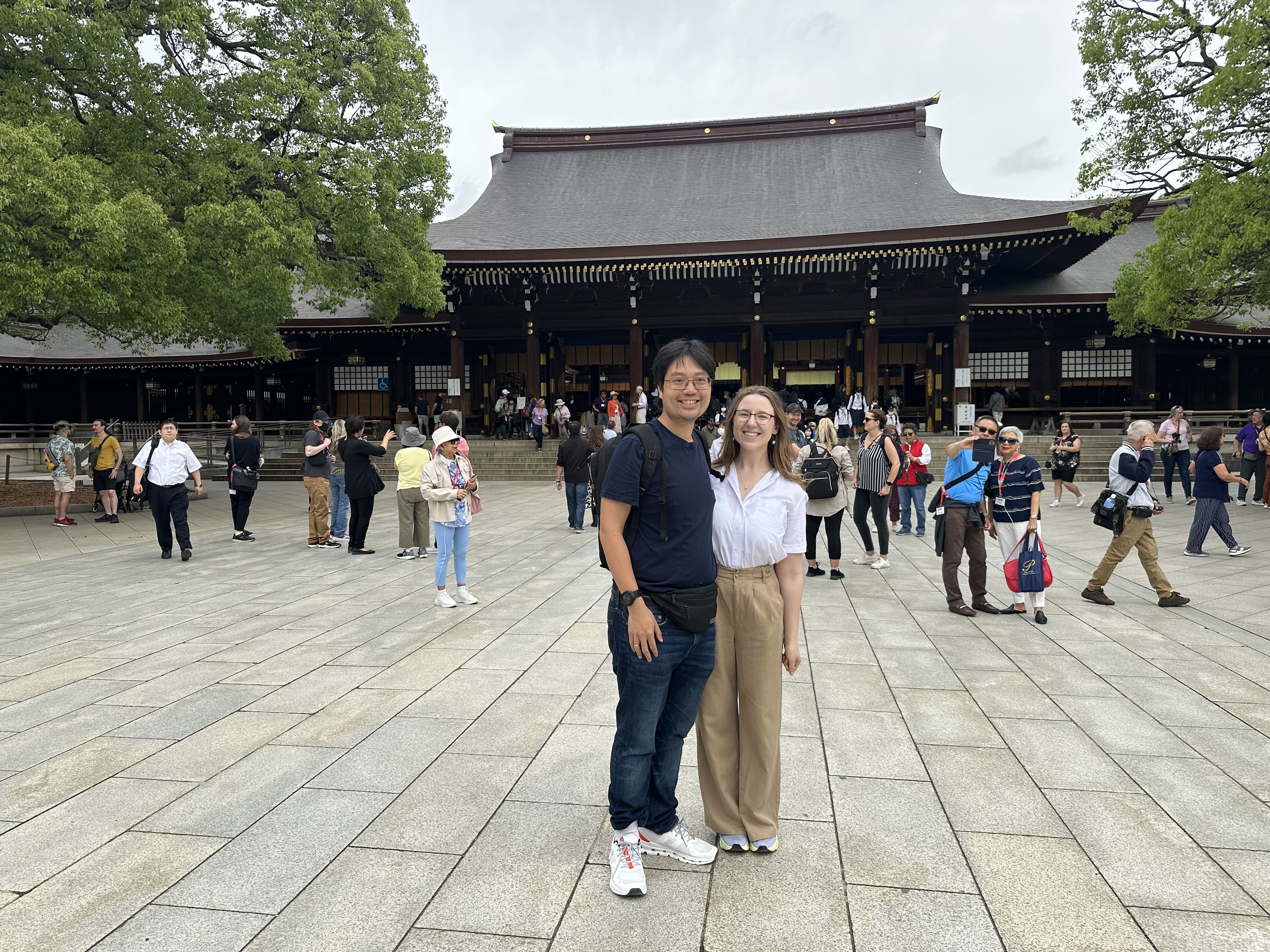 Mari-Alina Timoshchuk and Cassidy Sung in Tokyo in front of a large temple with many people in the background. It's a nice day. Mari-Alina Timoshchuk is wearing long brown pants and a white blouse.
