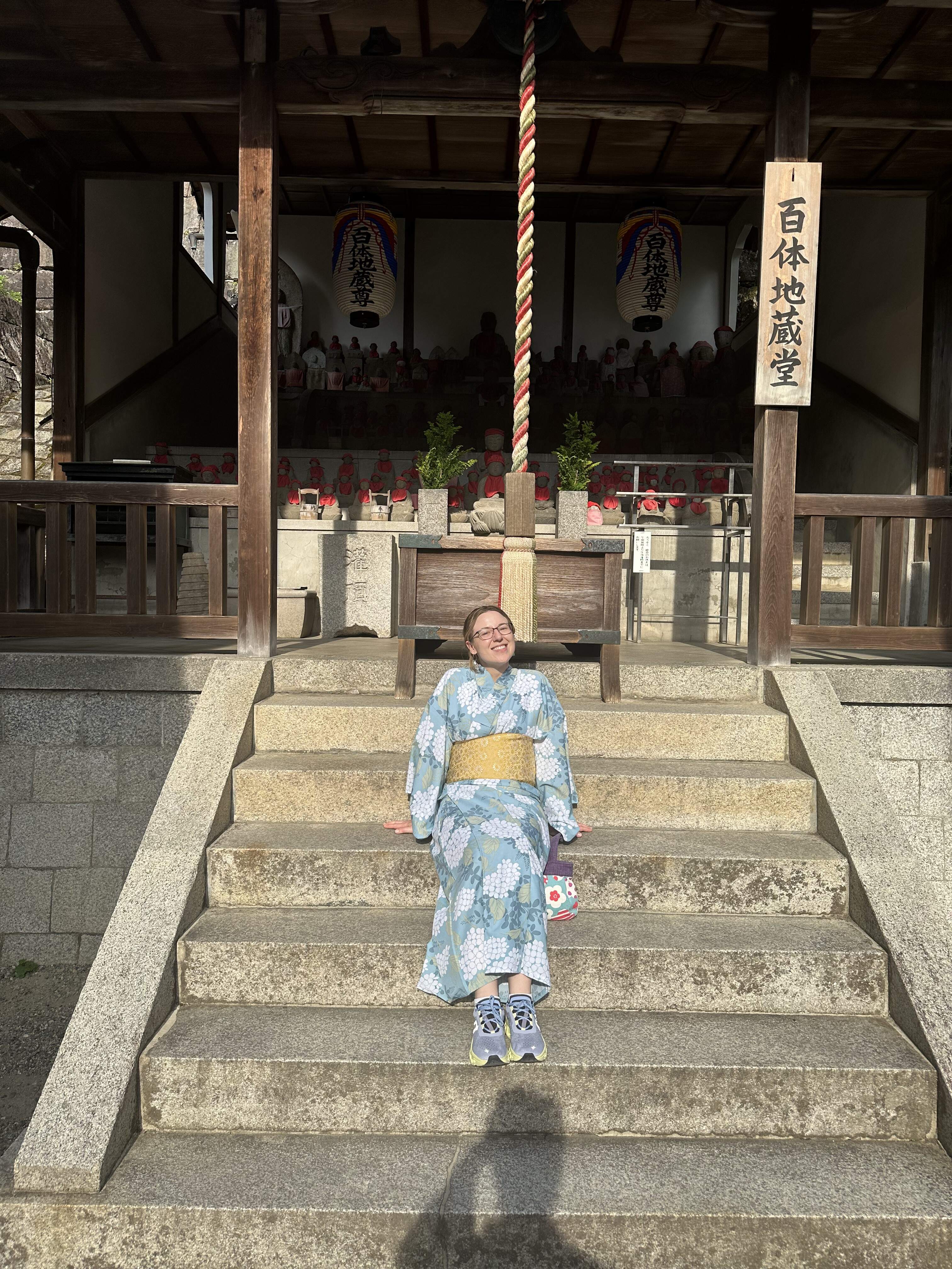 Mari-Alina Timoshchuk in the sun on the steps of a Japanese temple in a blue kimono smiling up at the sky 