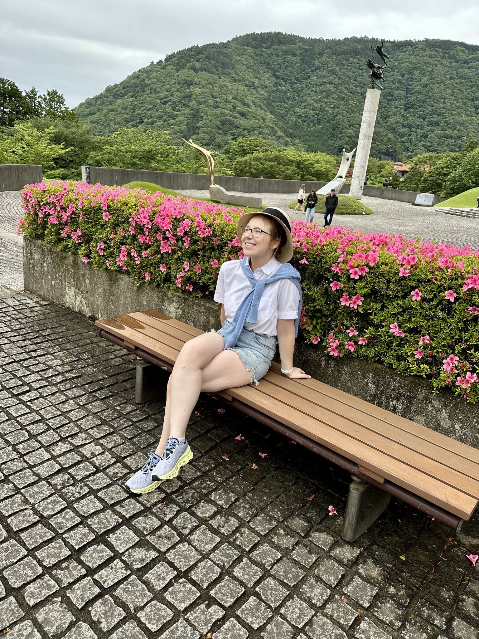 Mari-Alina Timoshchuk sitting at a bench at a statue museum in Japan with a flower bush in the background. 