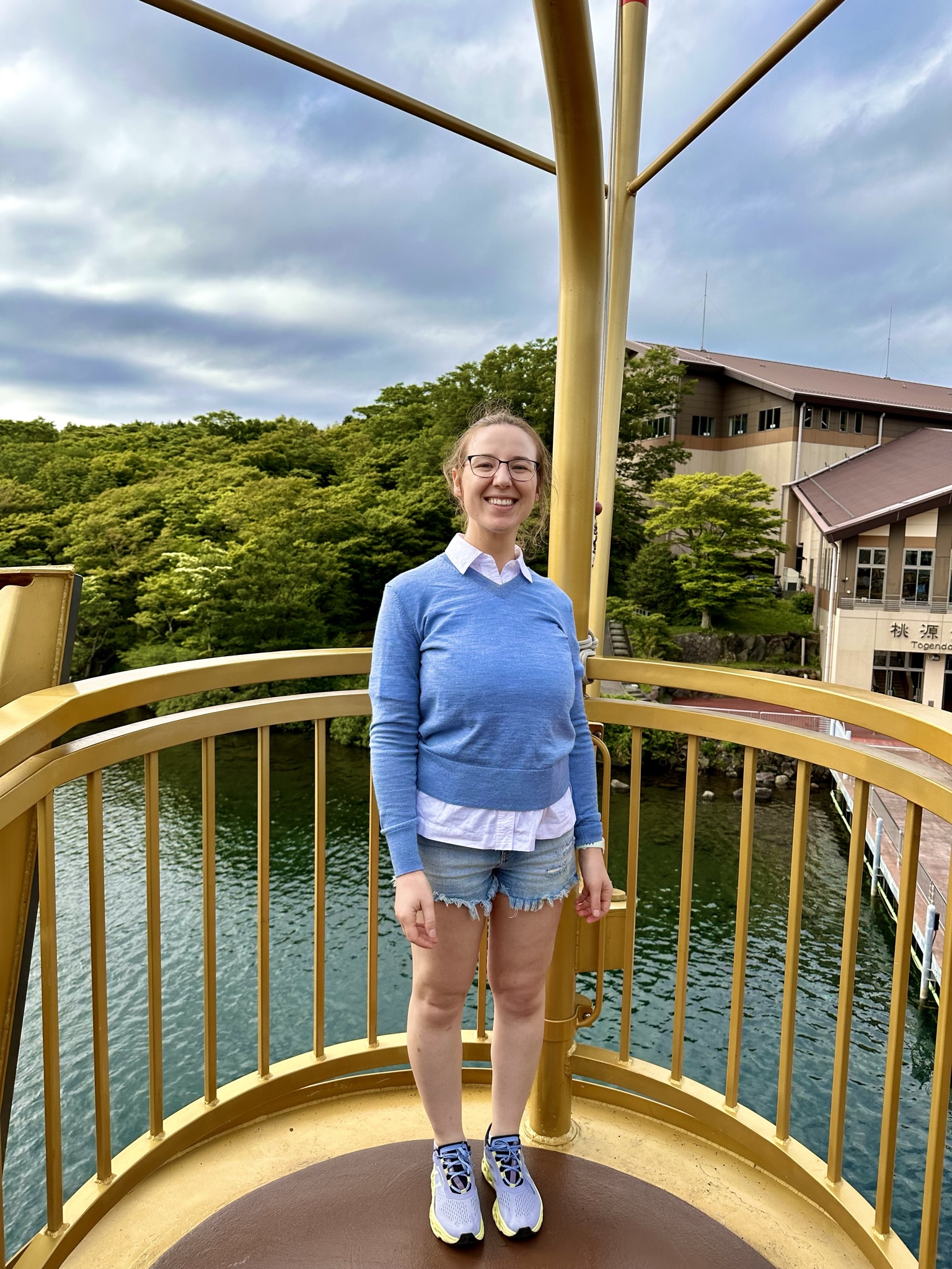 Mari-Alina Timoshchuk standing at the helm of a pirate ship in Japan . She is smiling. She is wearing a blue sweater and shorts. 