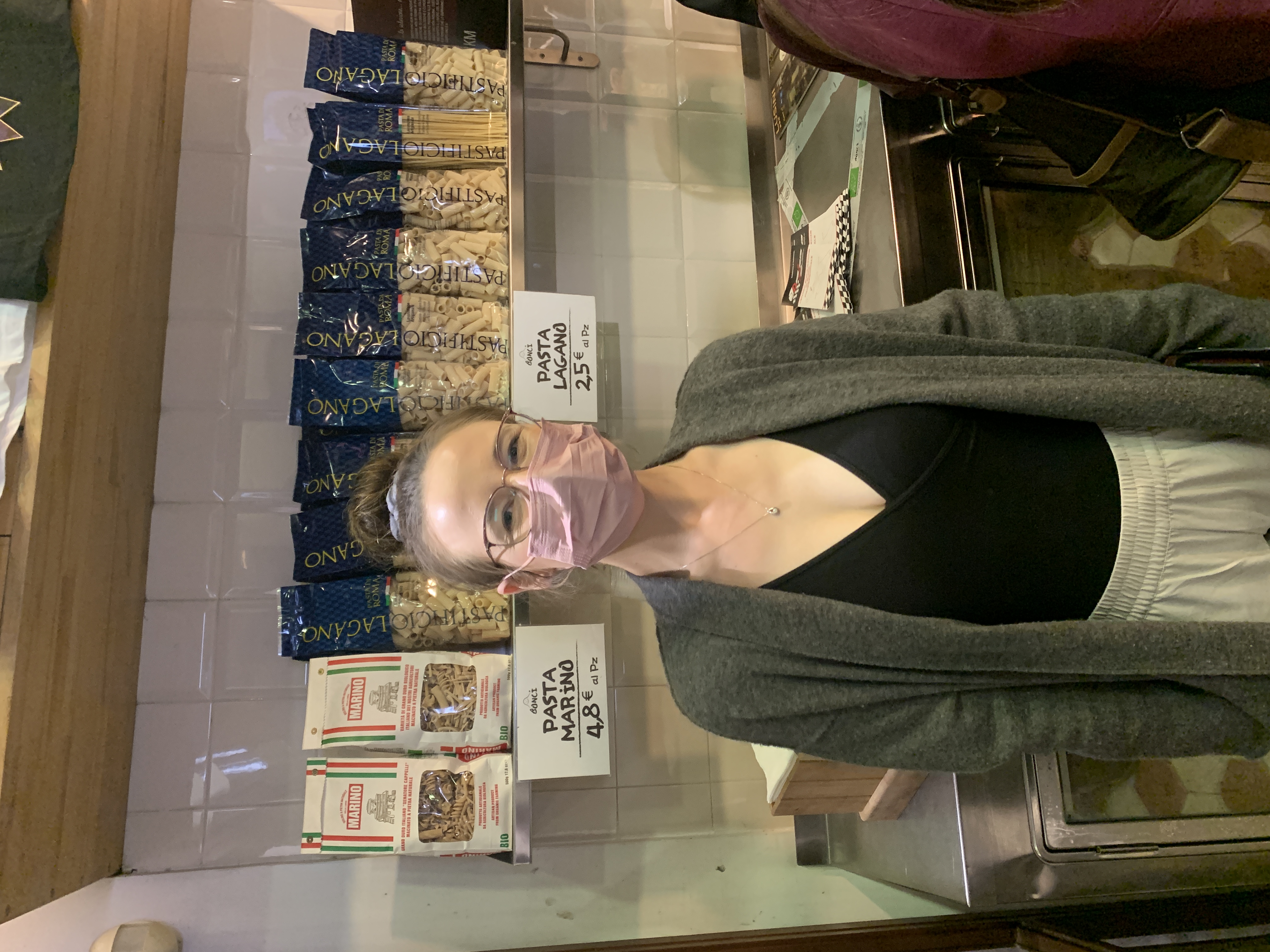 Mari-Alina Timoshchuk in a pizza shop in Rome with a pink mask and a long grey coat with a black shirt