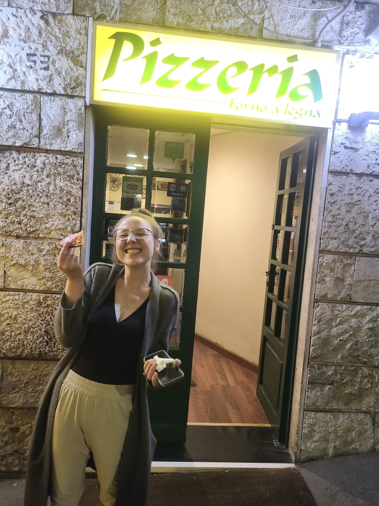 Mari-Alina Timoshchuk smiling and eating a piece of pizza in Rome