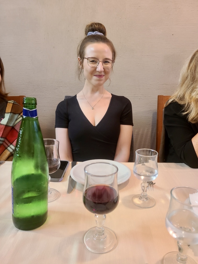 Mari-Alina Timoshchuk at a table in Rome with a large glass of red wine in front of her. Her hair is in a bun. 