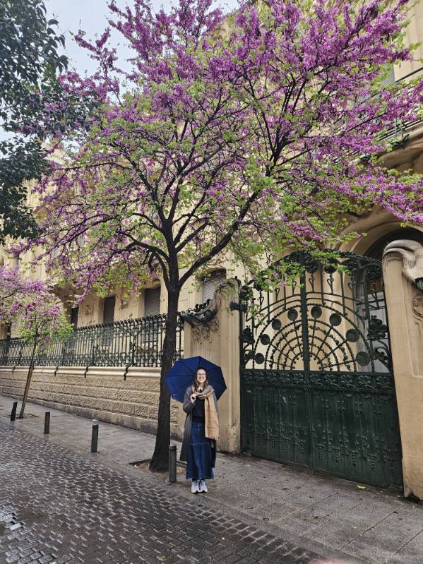 Mari-Alina Timoshchuk standing under a tree with purple flowers in Madrid Spain holding an umbrella