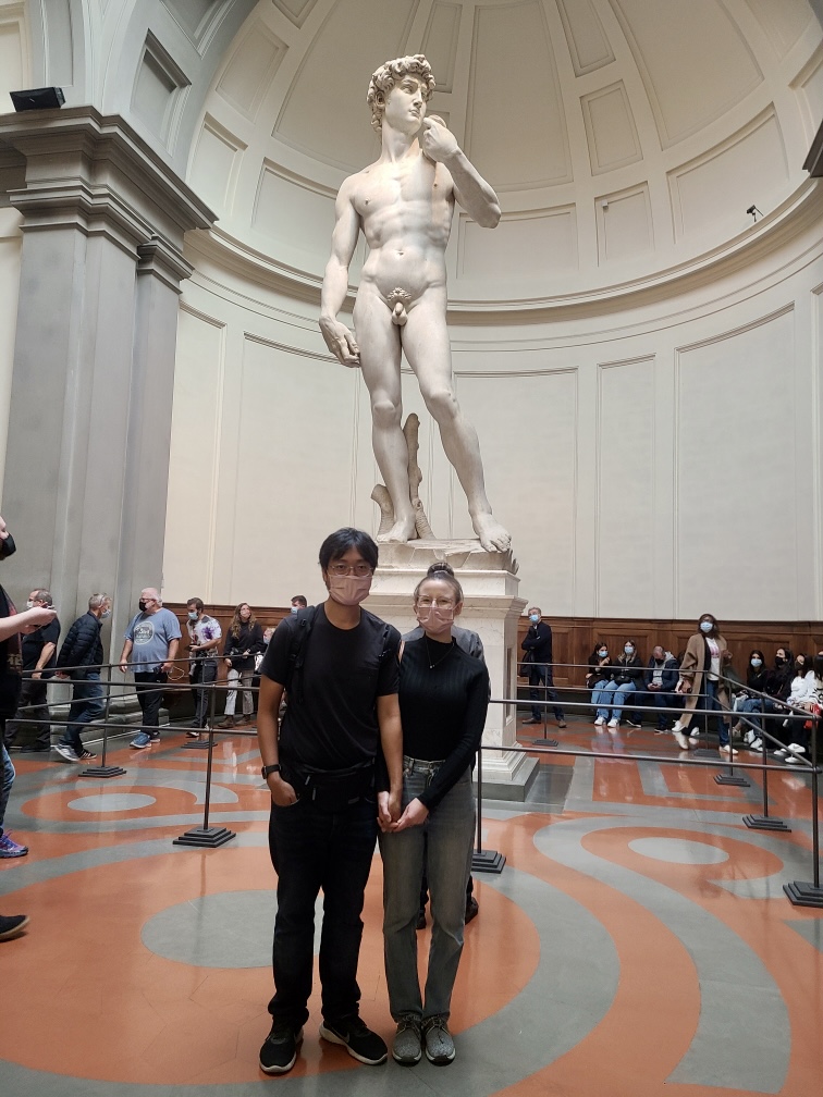 Mari-Alina Timoshchuk and Cassidy Sung in front of the statue of David in Florence Italy. The are holding hands. 