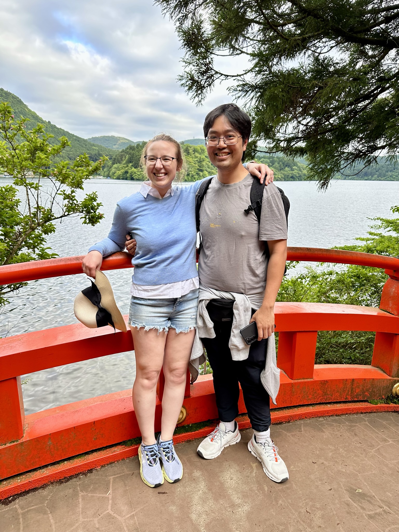 Mari-Alina Timoshchuk and Cassidy Sung standing on the bridge that is red next to a Japanese shrine. There is water and trees in the background