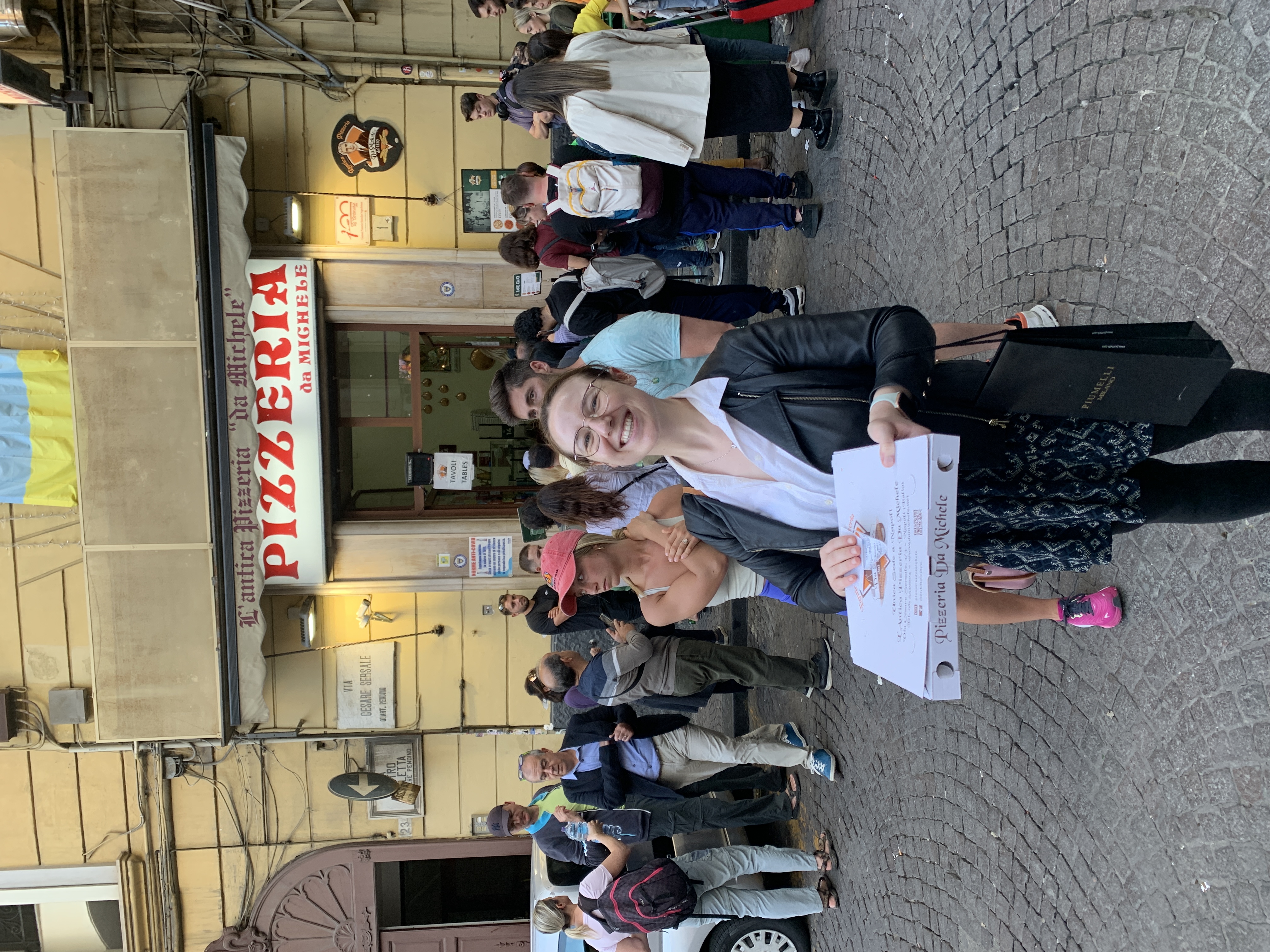 Mari-Alina Timoshchuk in front of a famous pizza place in Naples Italy holding a box of pizza