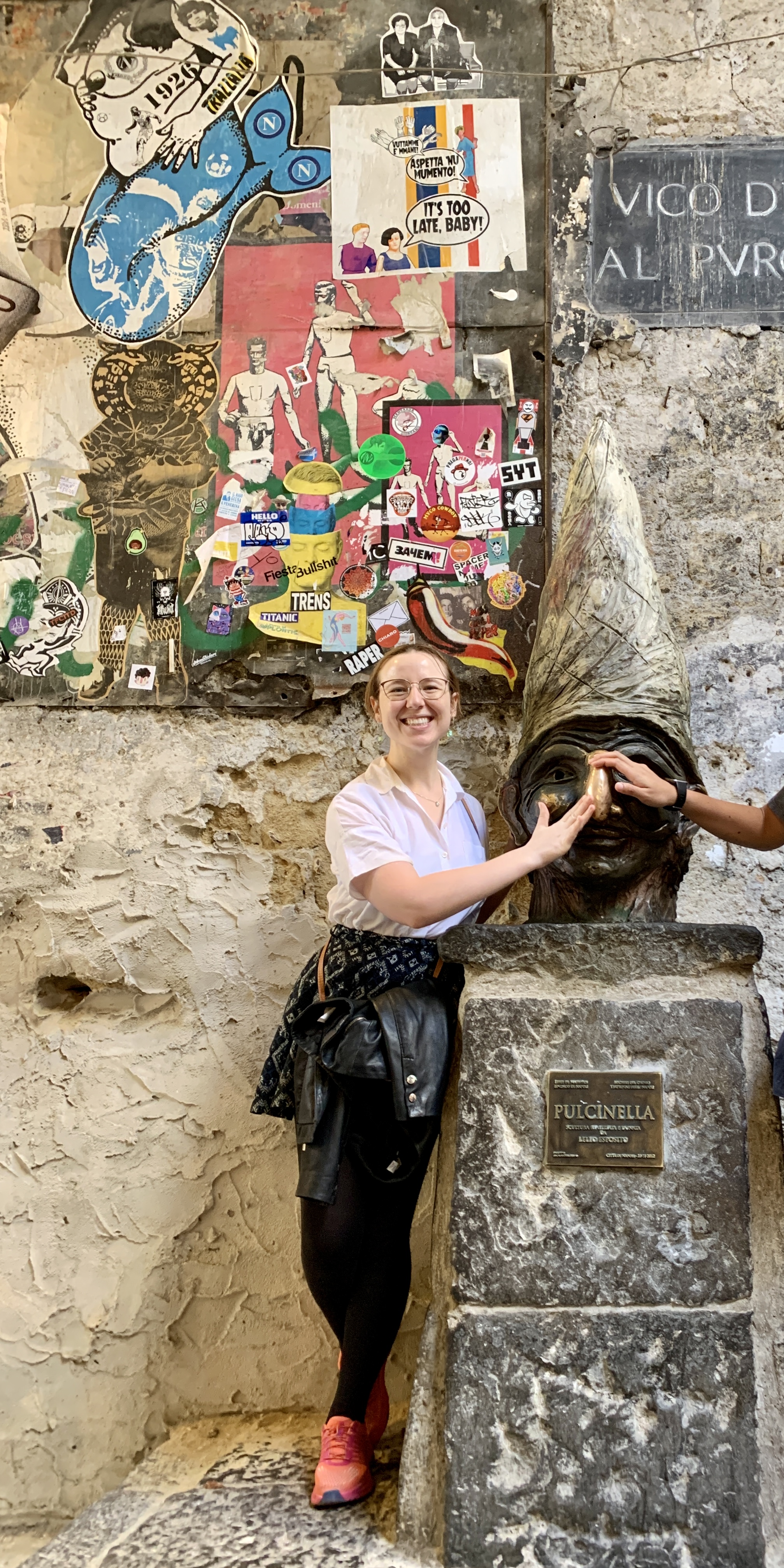 Mari-Alina Timoshchuk touching the nose of Pulcinella in Naples Italy in front of a wall with graffiti