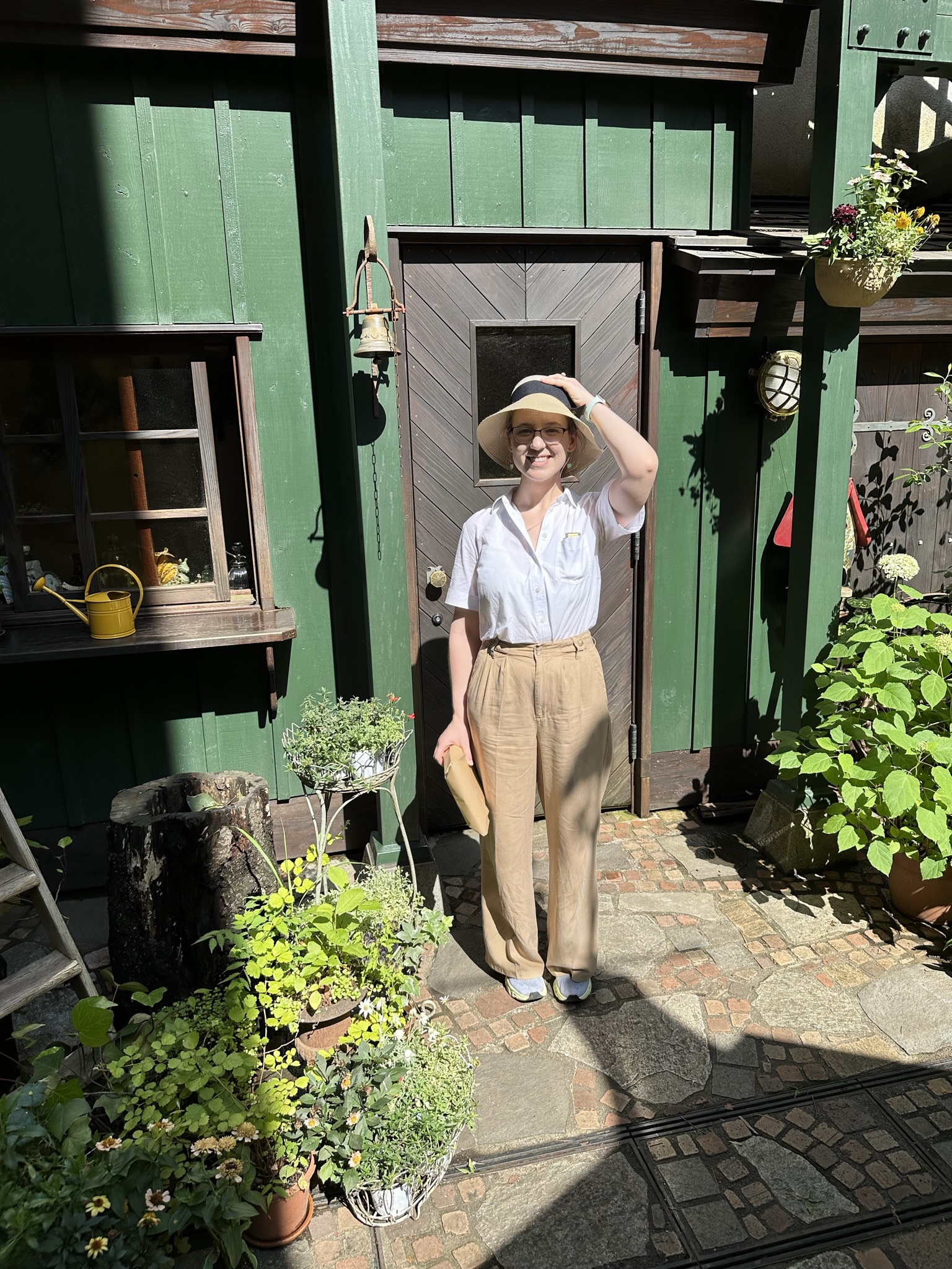 Mari-Alina Timoshchuk at the Studio Ghibli museum next to a green door with a hand on her hat carrying a parcel