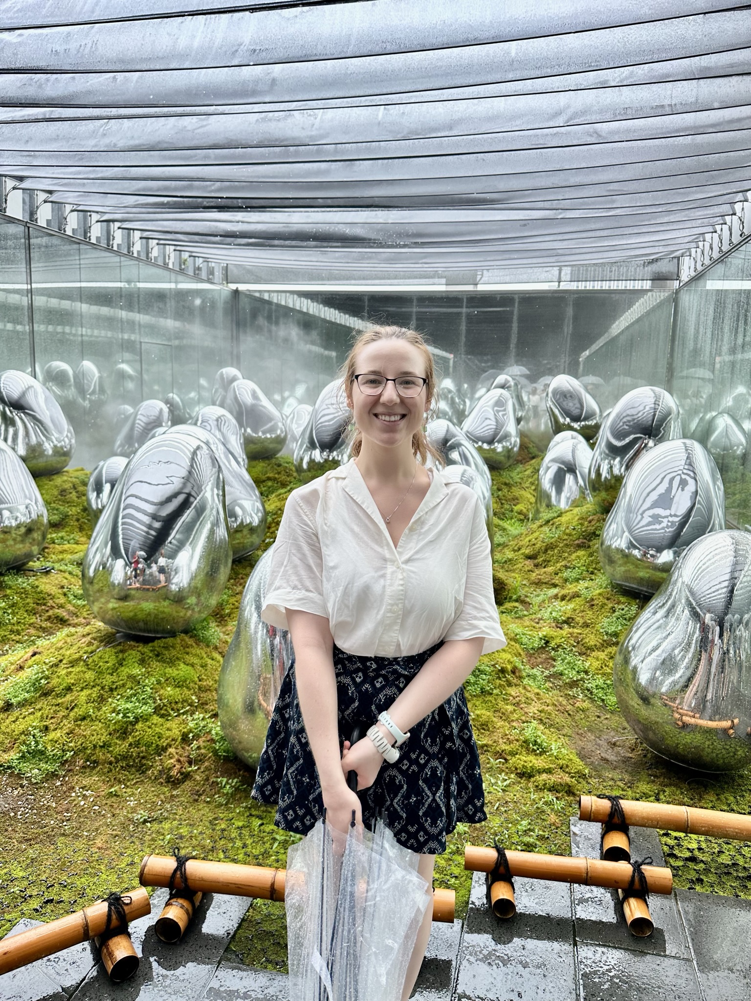 Mari-Alina Timoshchuk at Team Labs Planets in Tokyo next to a lot of statues and moss holding an umbrella