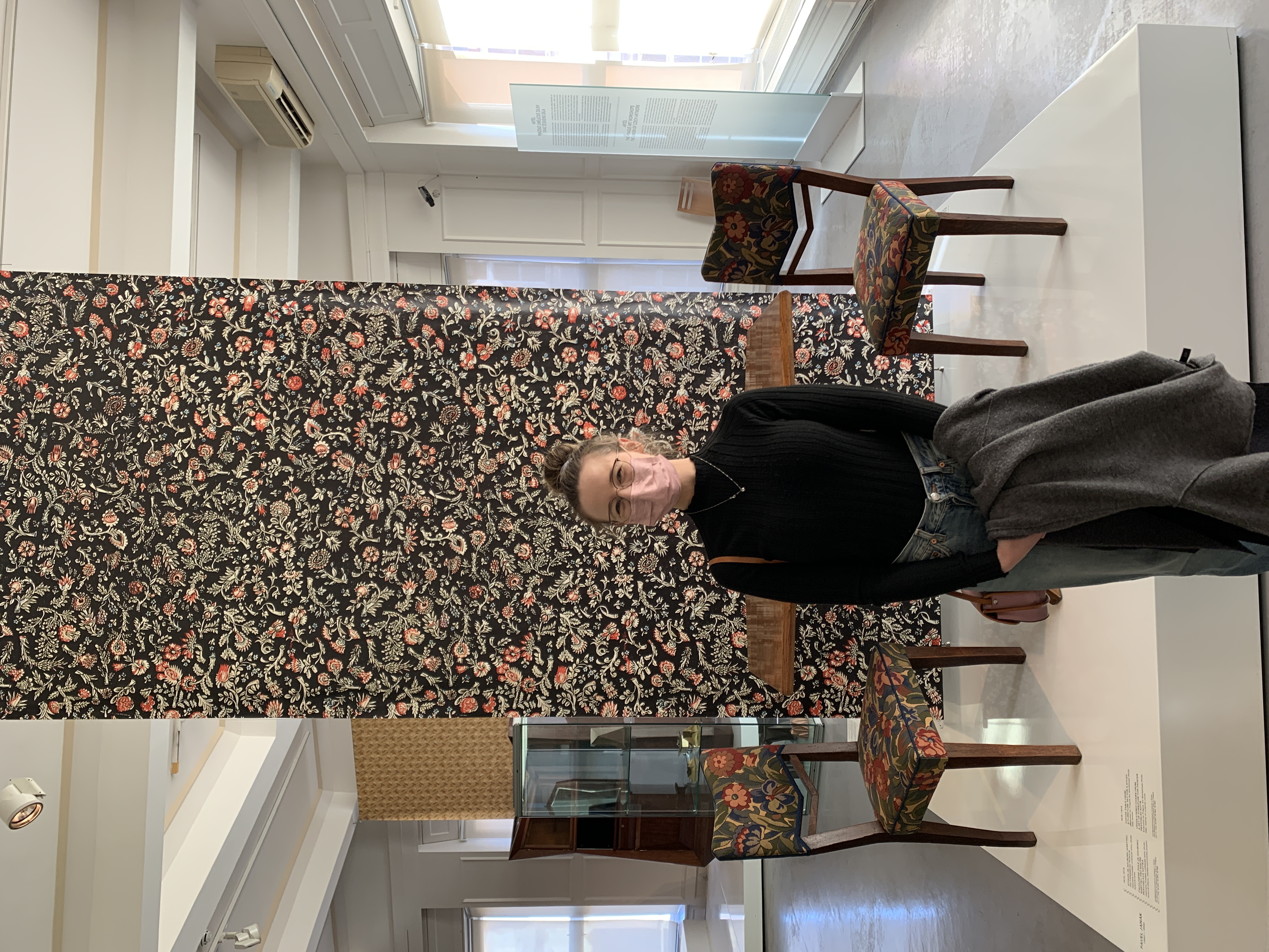 Mari-Alina Timoshchuk in the Cubism museum in Prague next to a floral wall and chairs