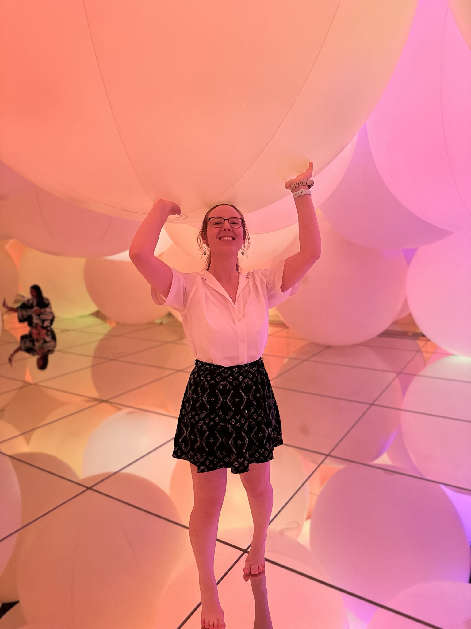 Mari-Alina Timoshchuk at teamLabs planets holding a large sphere that has a pink tinge of color with other spheres in the background. 