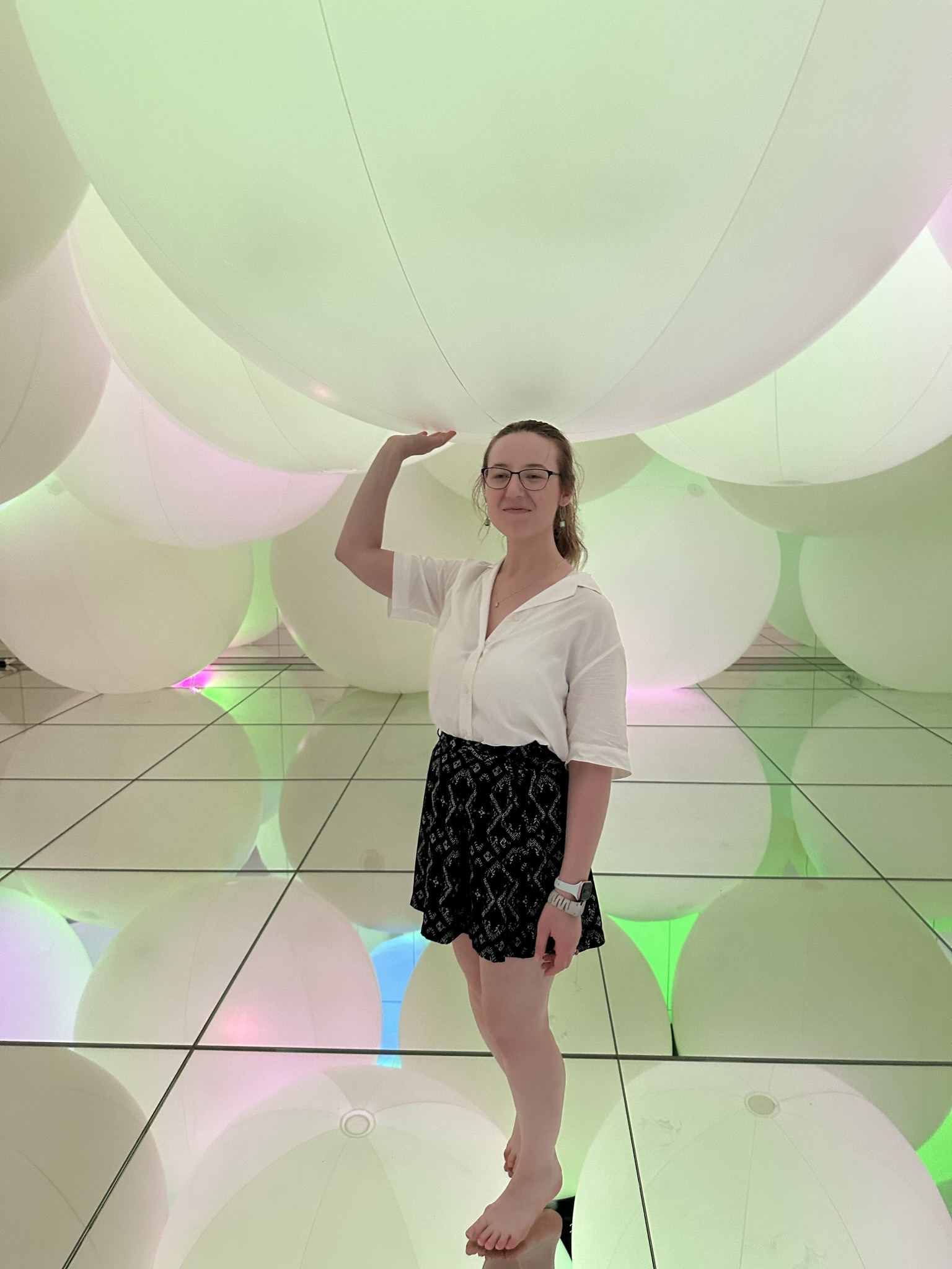 Mari-Alina Timoshchuk at a modern art museum in Tokyo surrounded by white spheres holding up a sphere. 