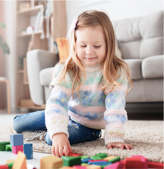 Young girl playing with colorful building blocks on a rug.
