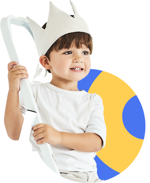Smiling boy wearing a white crown, holding a white object.