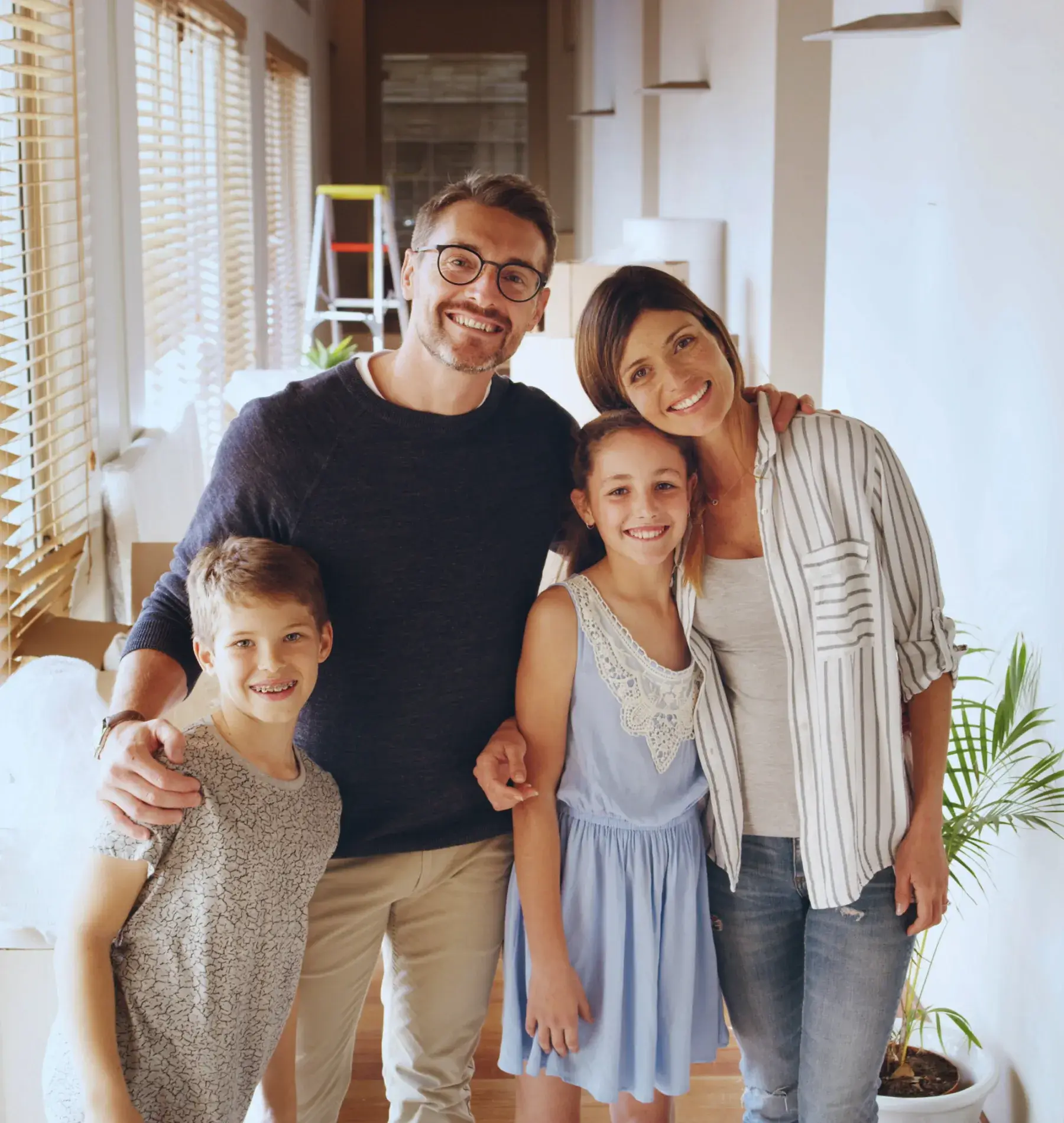 A smiling family of four poses together inside a well-lit room.
