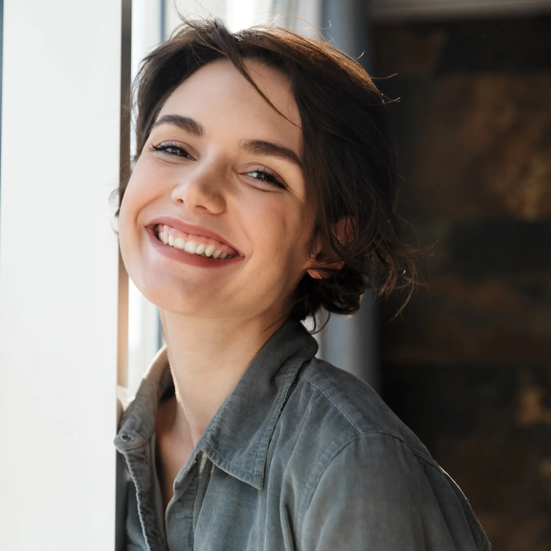 A person smiling brightly while standing near a window.