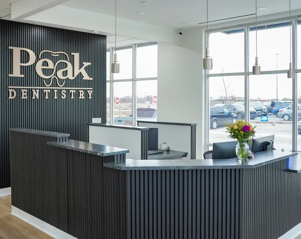 Modern dental office reception with dark wood counter, large windows, and Peak Dentistry logo on the wall.