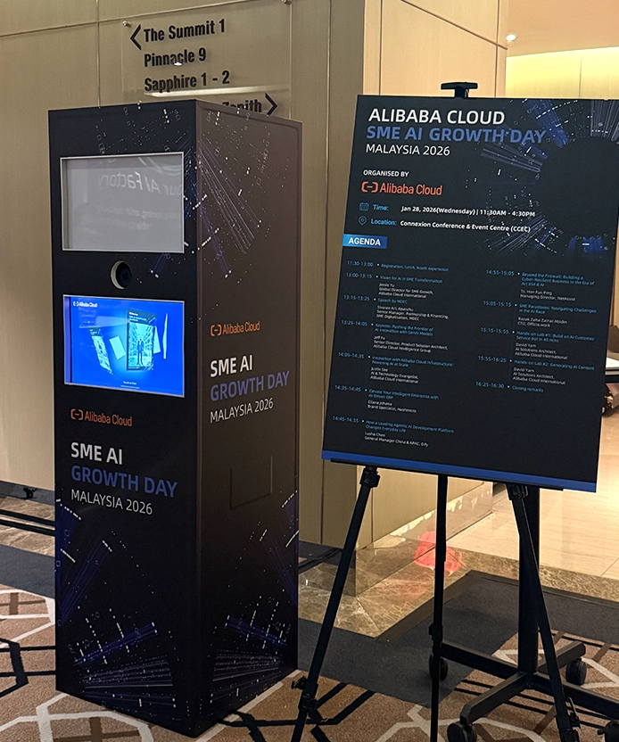 Alibaba Cloud SME AI Growth Day kiosk beside the event signage board.