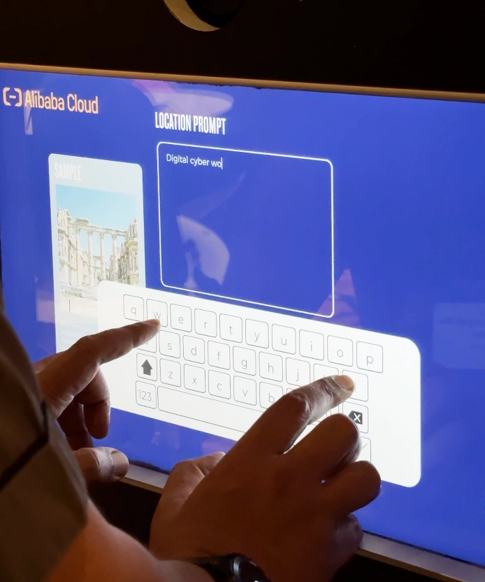 Close-up of hands typing a location prompt on the Alibaba Cloud touchscreen keyboard.