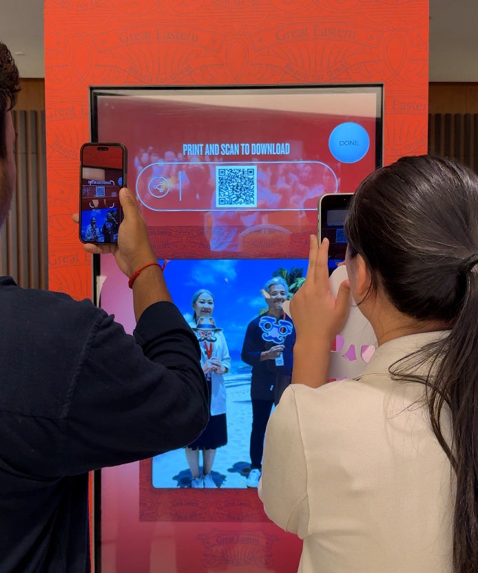 Two people photographing the kiosk screen with their smartphones.