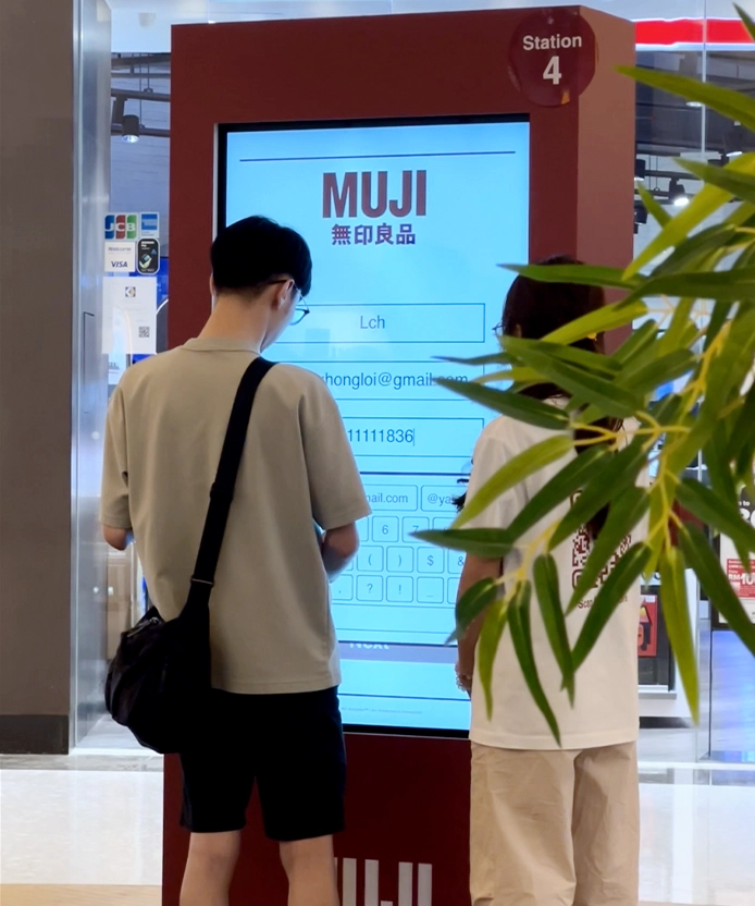 Shoppers browsing the MUJI kiosk touchscreen interface.