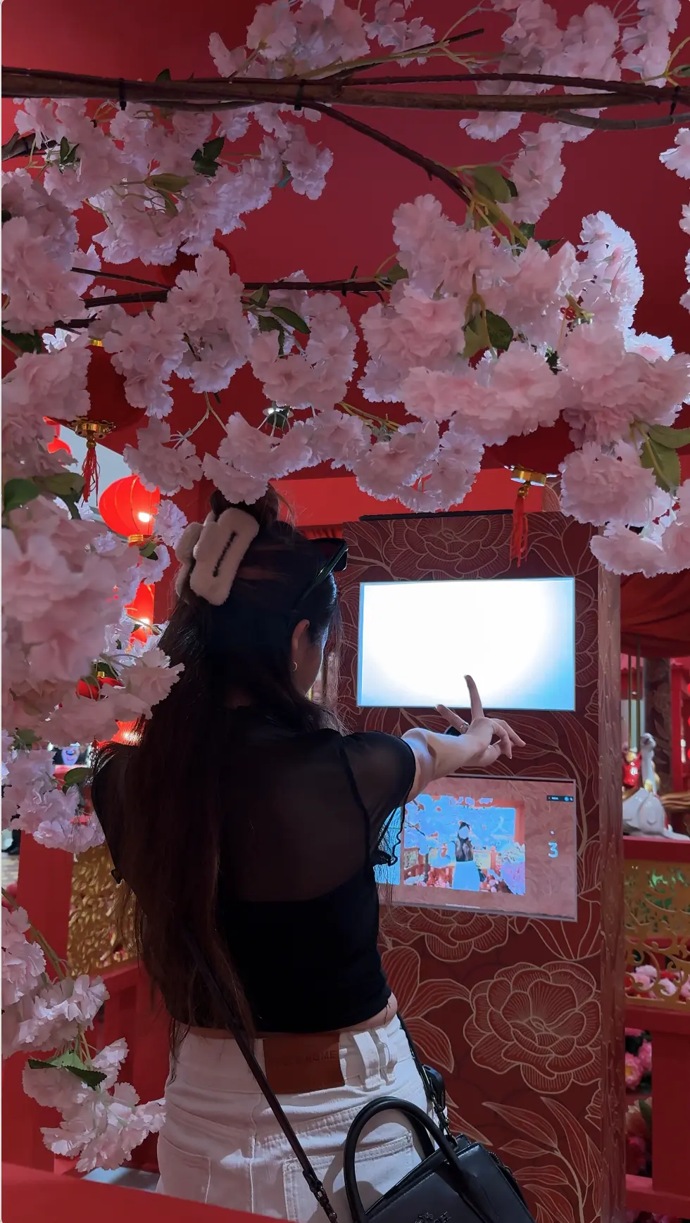 Visitor pointing and posing for the camera at the Suria KLCC Chinese New Year photo booth under a canopy of pink cherry blossoms