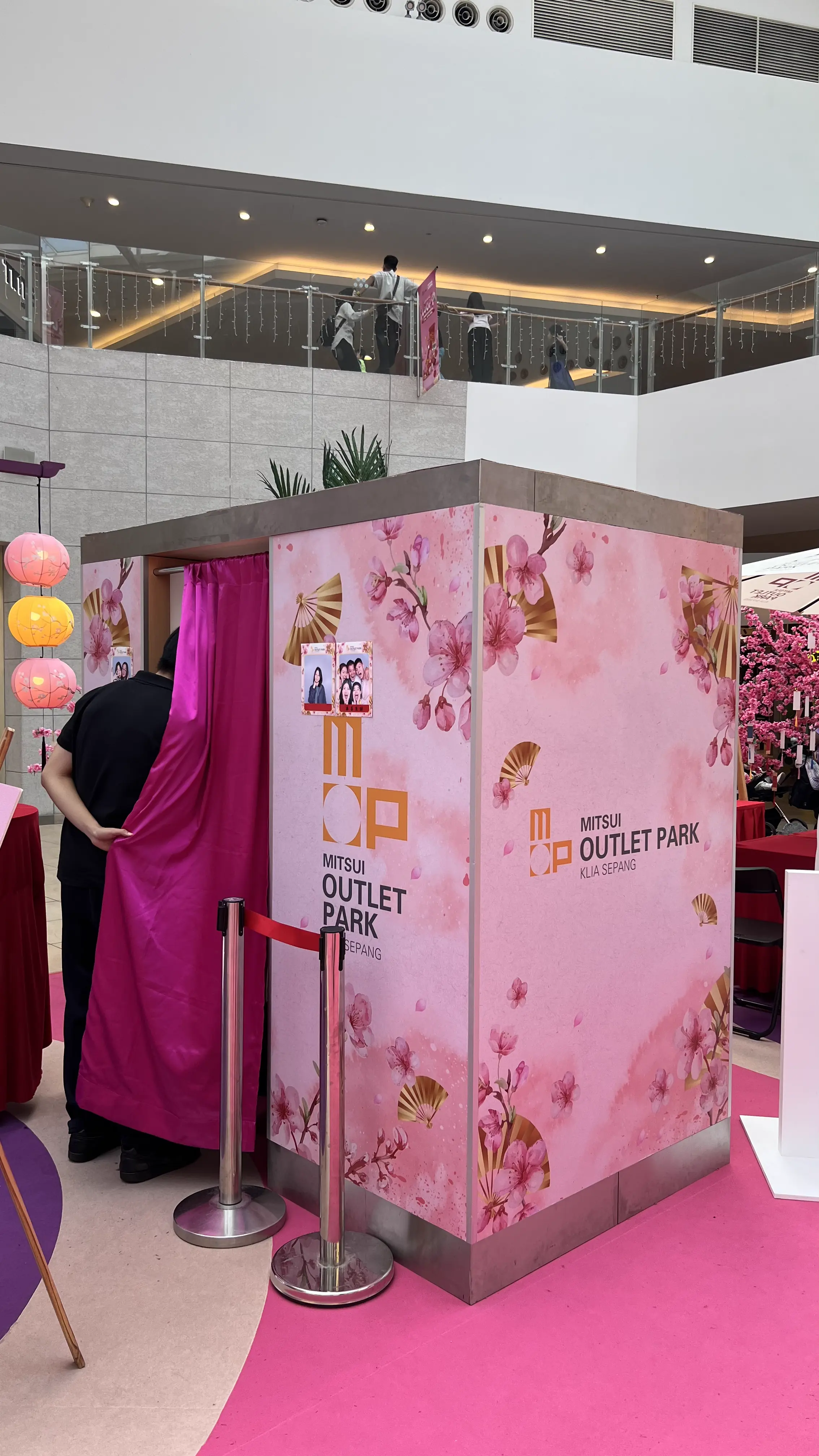 Cherry blossom–themed Mitsui Outlet Park KLIA Sepang calligraphy photo booth with pink curtain entrance and hanging lanterns in the mall atrium