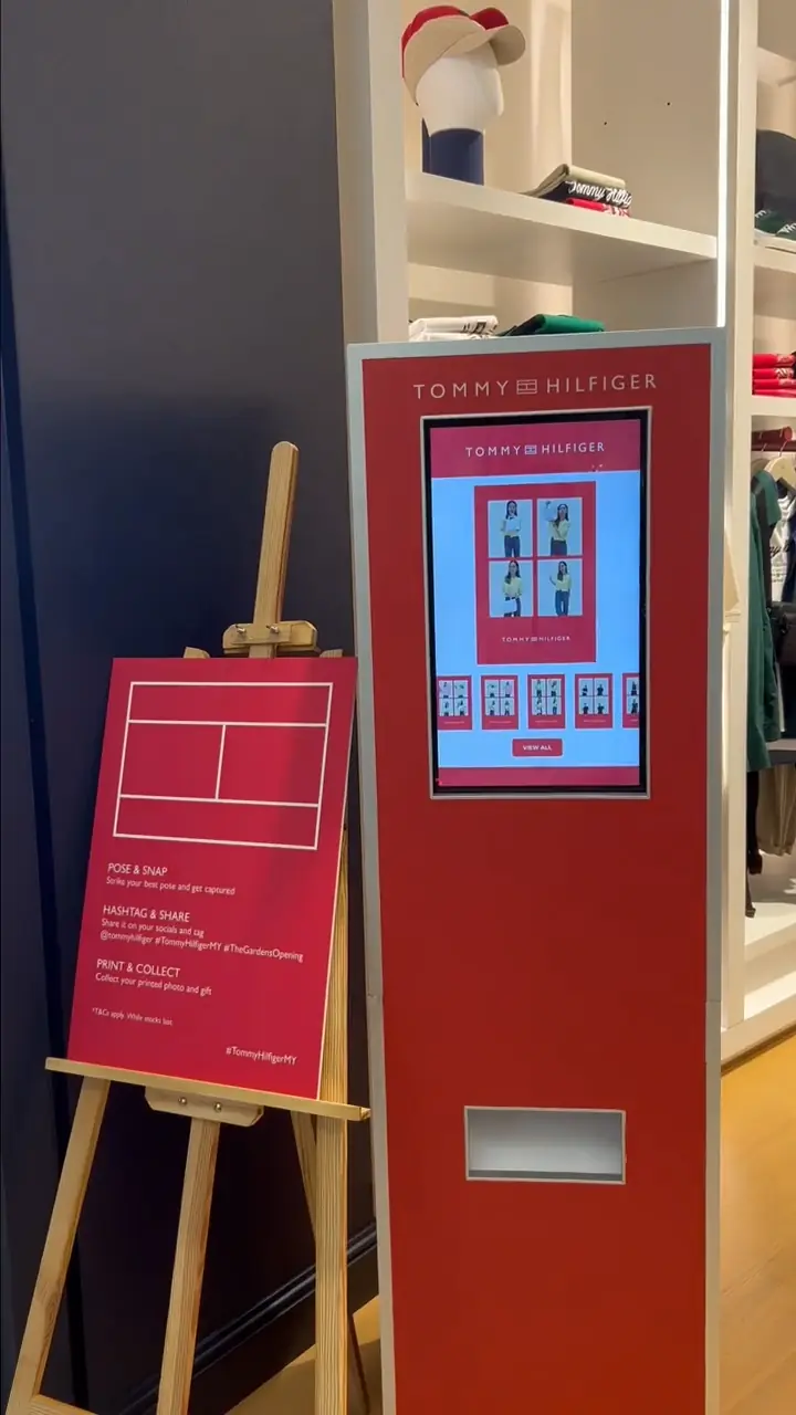 Red Tommy Hilfiger photo booth kiosk with touch screen and "Pose & Snap" instructions easel at the Garden Mall store opening