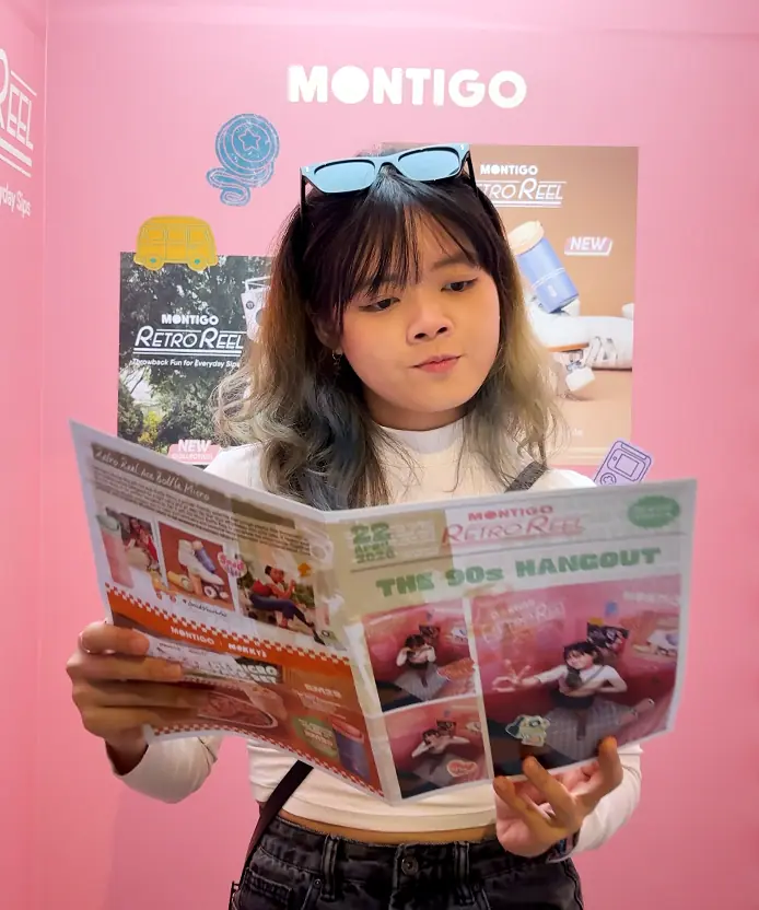 Guest reading her printed Montigo Retro Reel newspaper photo strip in front of the branded pink backdrop