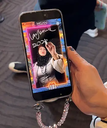 Hand holding a phone showing the downloaded glowing signature video from the MGAN glass drawing booth