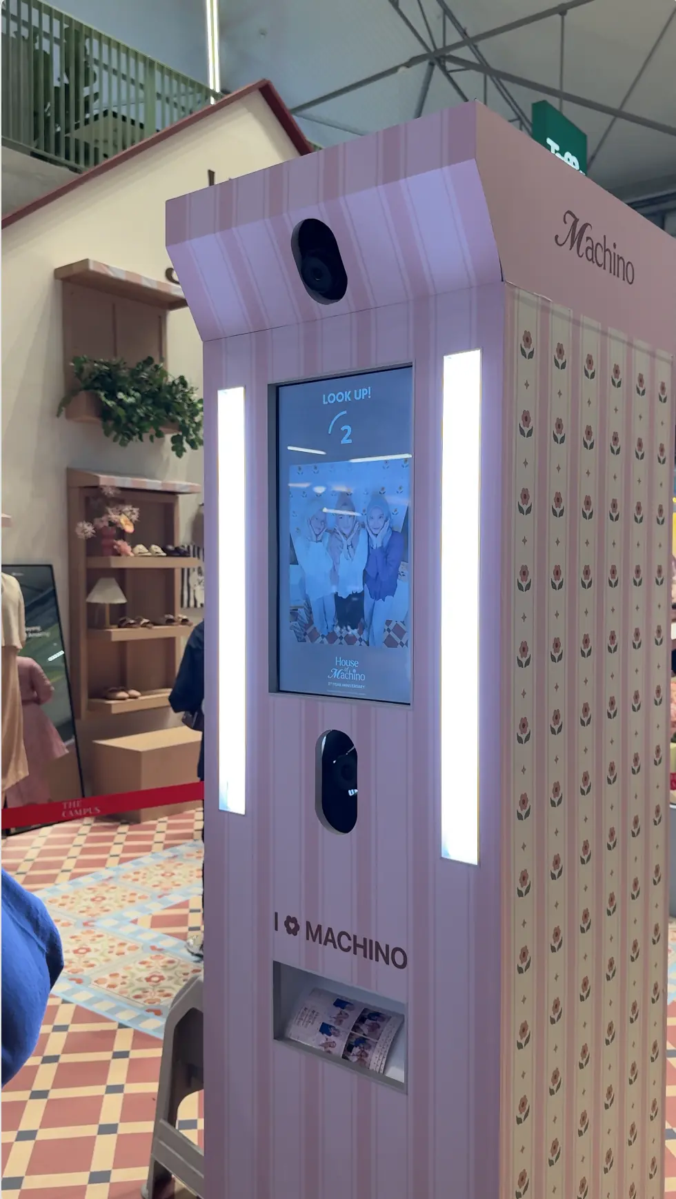 Close-up of the pink floral House of Machino photo booth showing the "Look Up!" countdown screen and a printed photo strip in the dispenser