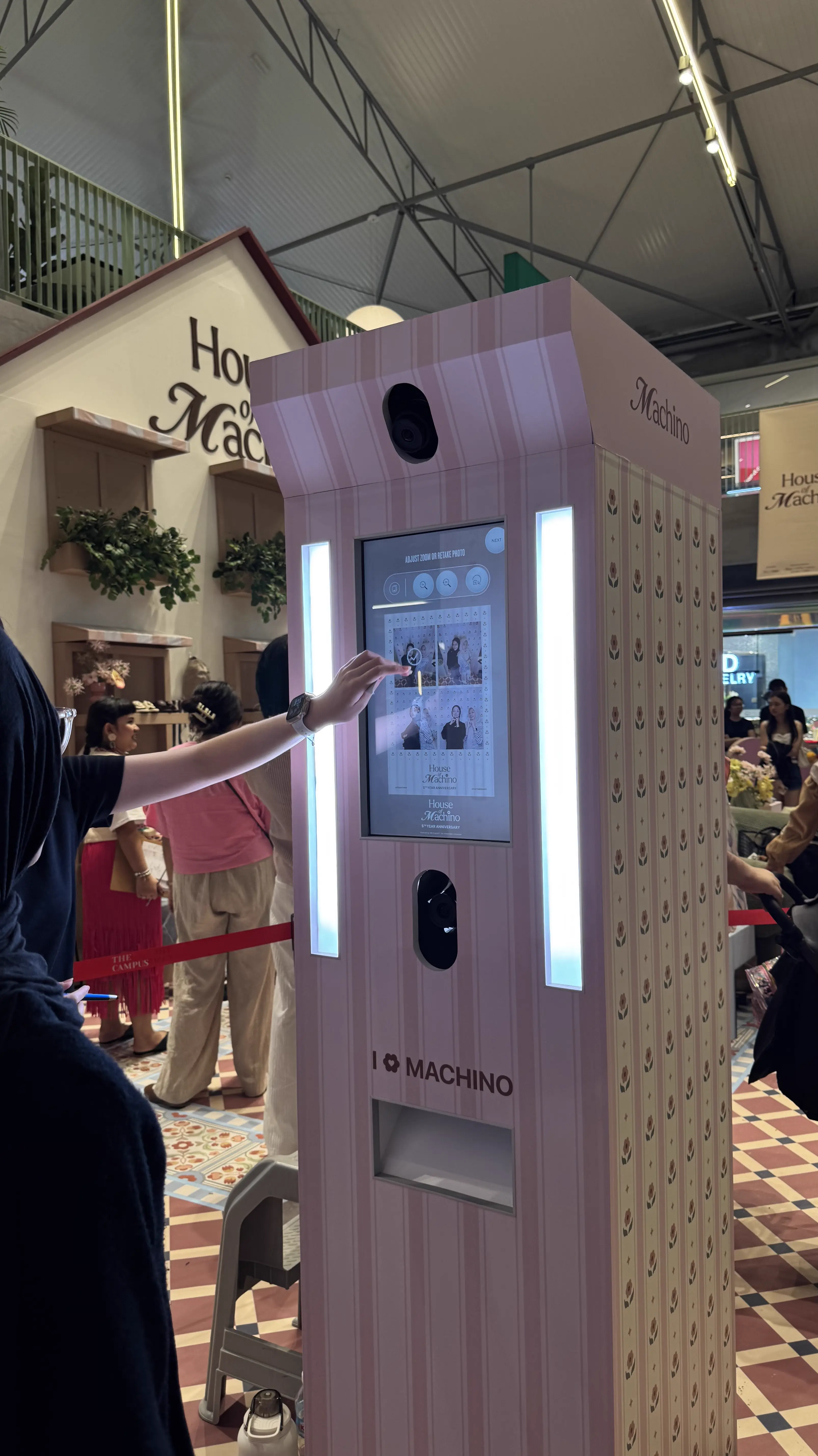 Visitor reaching to tap the touchscreen of the pink striped House of Machino photo booth at the brand's pop-up event