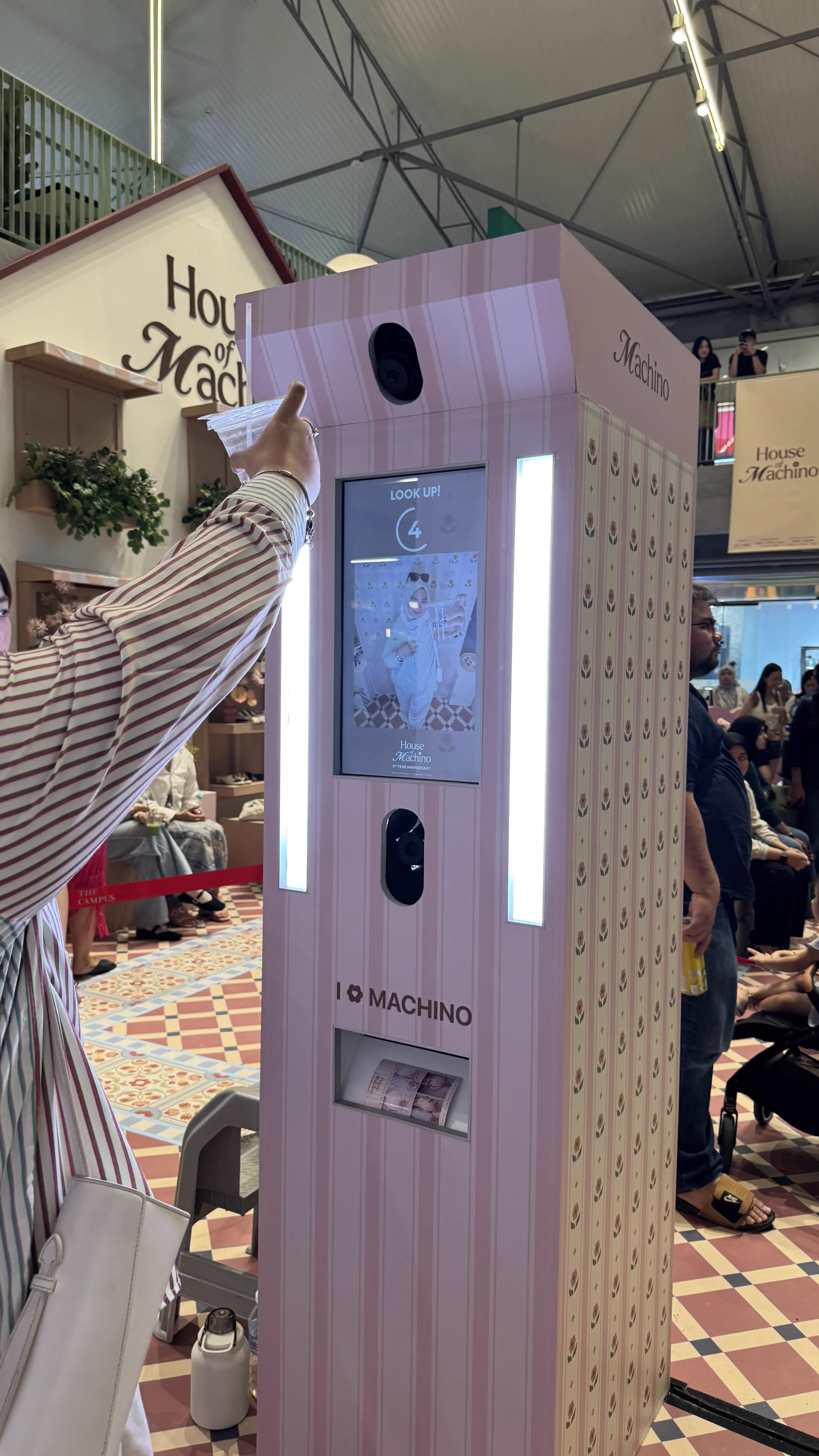 Visitor pointing at the House of Machino photo booth screen as it counts down, inside the brand's pink-themed pop-up space