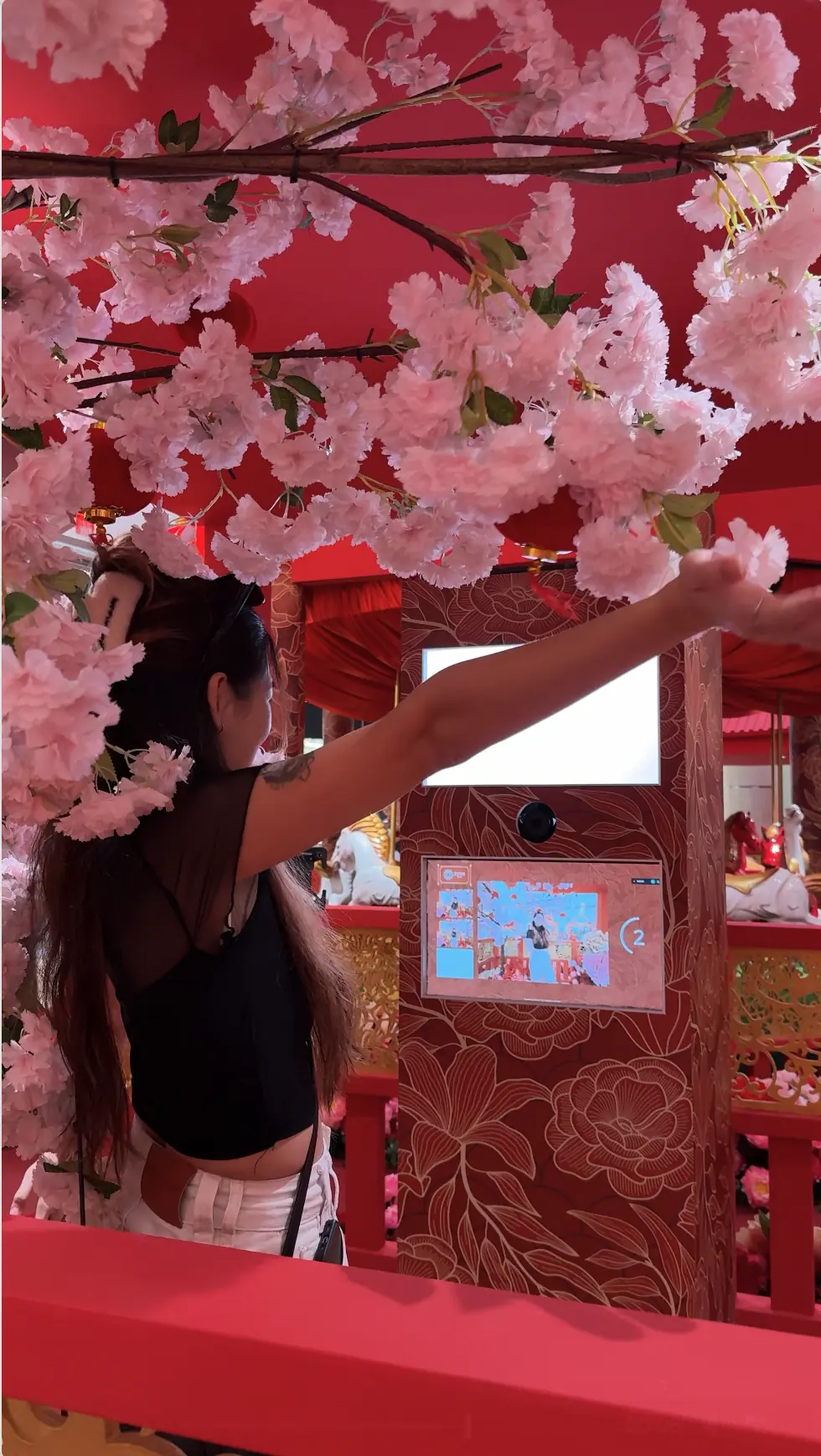 Woman reaching toward cherry blossoms at the Suria KLCC CNY photo booth in Kuala Lumpur during a countdown