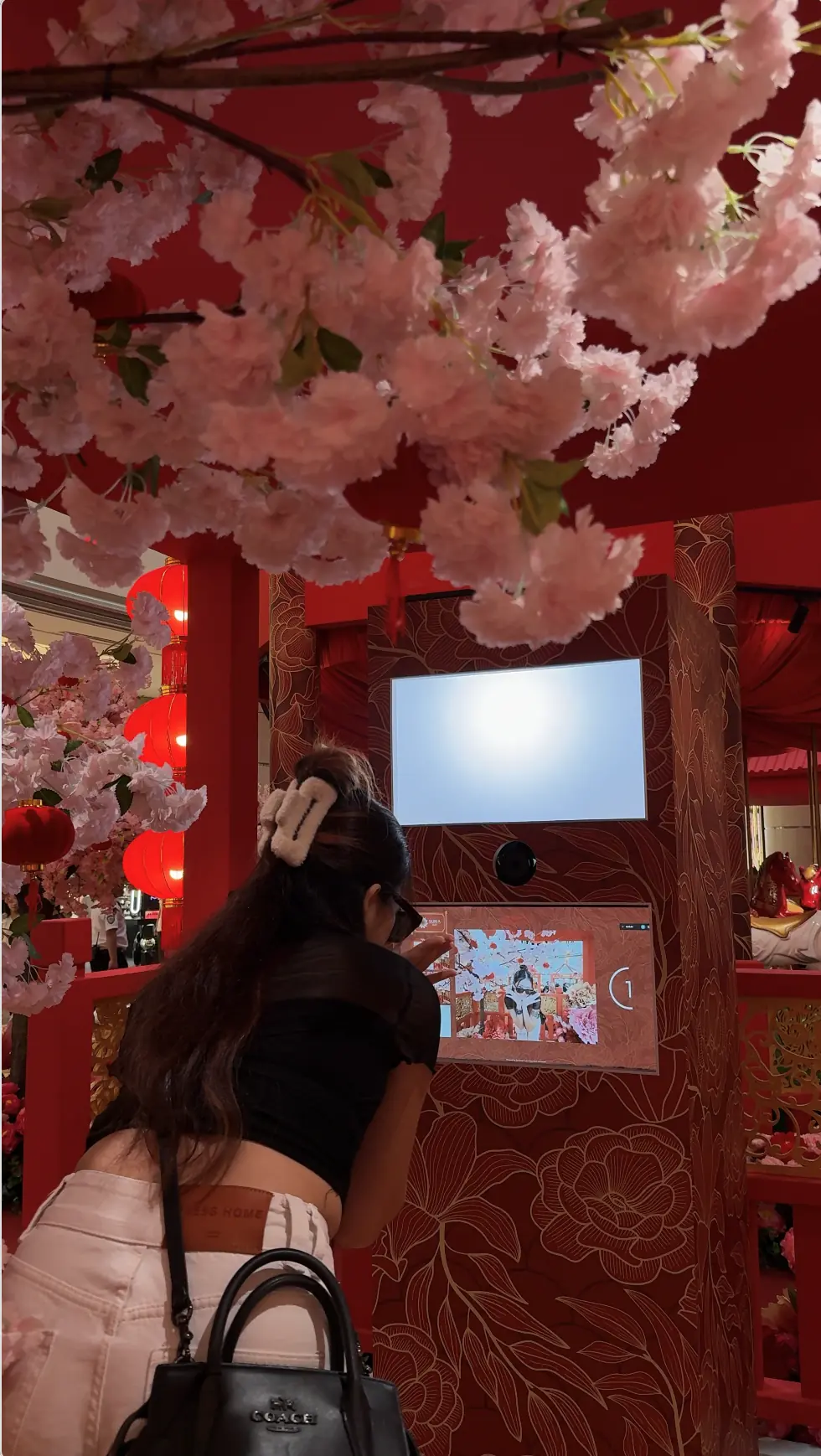 Visitor tapping the touchscreen to start the Suria KLCC CNY photo booth in Kuala Lumpur, framed by cherry blossoms