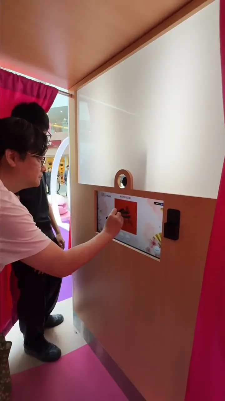 Visitor leaning into the Mitsui Outlet Park photo booth to draw on the Write Your Greeting calligraphy touchscreen