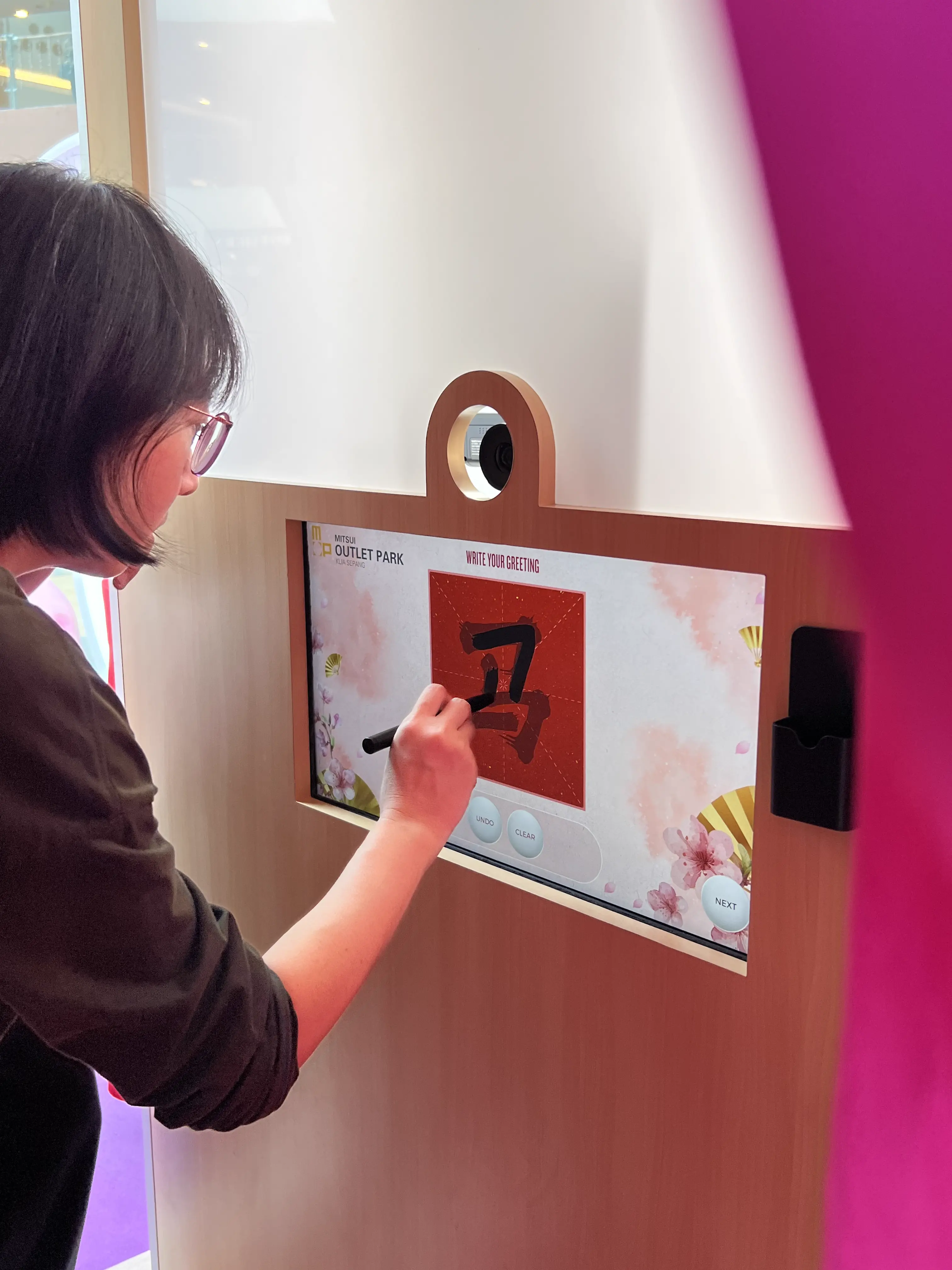 Visitor writing a Chinese calligraphy greeting with a stylus on the Mitsui Outlet Park booth's interactive screen