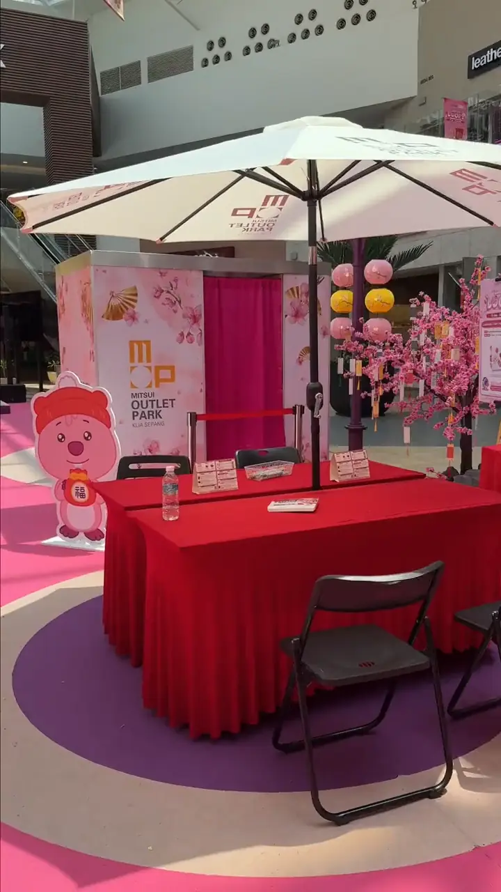 Mitsui Outlet Park KLIA Sepang Chinese New Year calligraphy booth with red-draped table, parasol, cherry blossom tree, lanterns and a Fuku bear mascot cutout