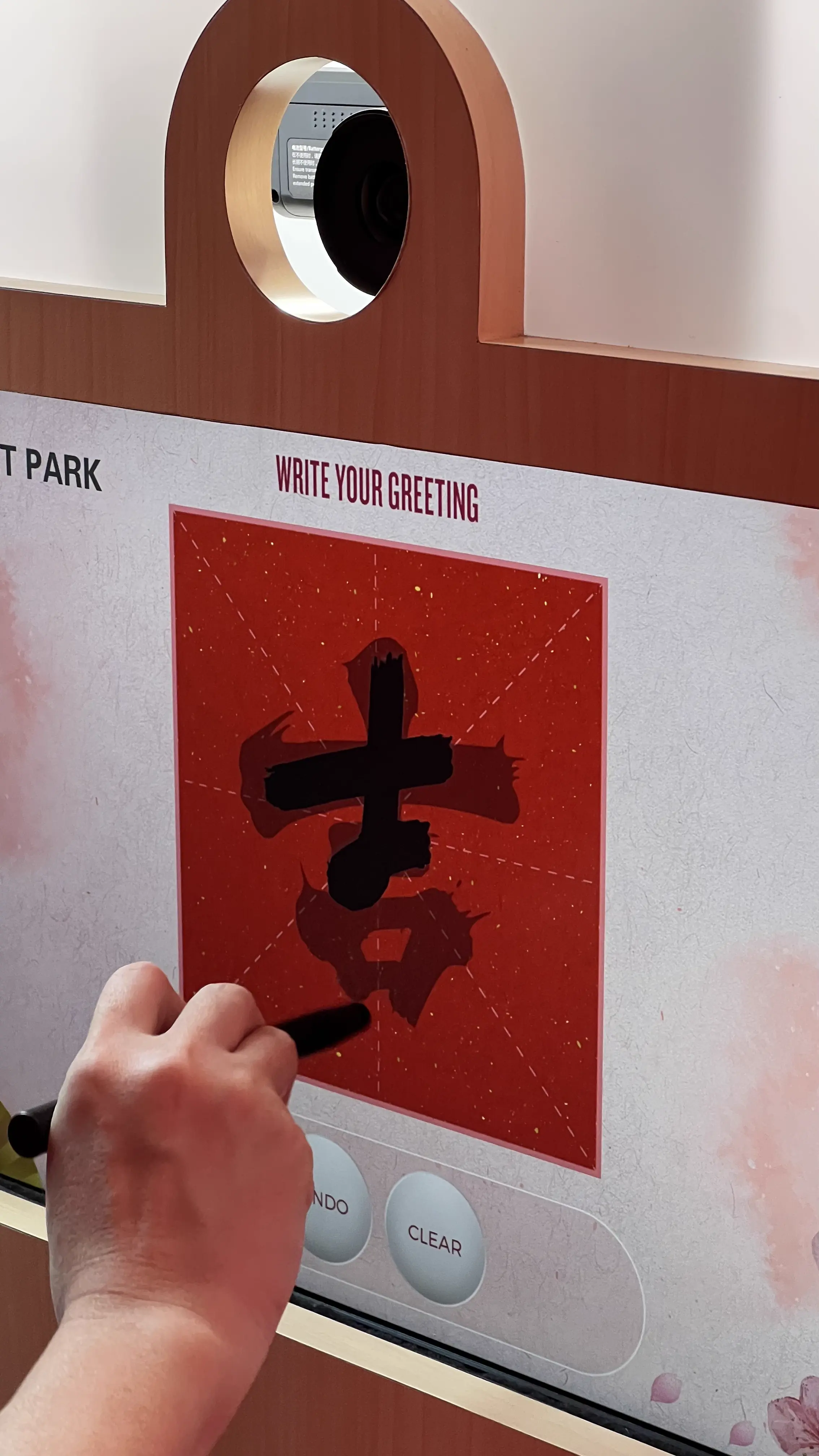 Hand using a stylus to write a Chinese New Year luck character on the Mitsui Outlet Park booth touchscreen