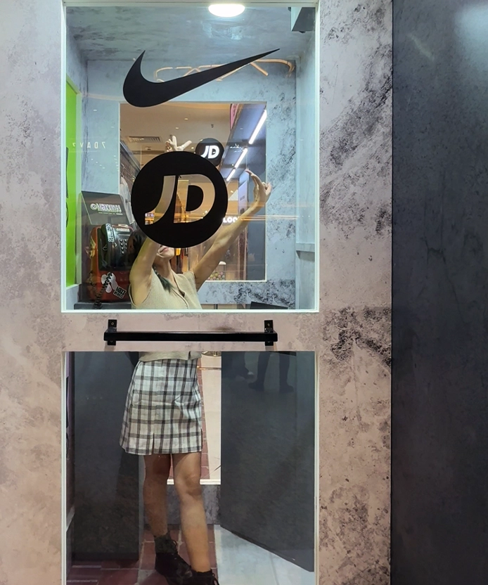 Guest posing with arms raised inside the Nike x JD Maxxin '95 high-angle phone booth window frame, Malaysia