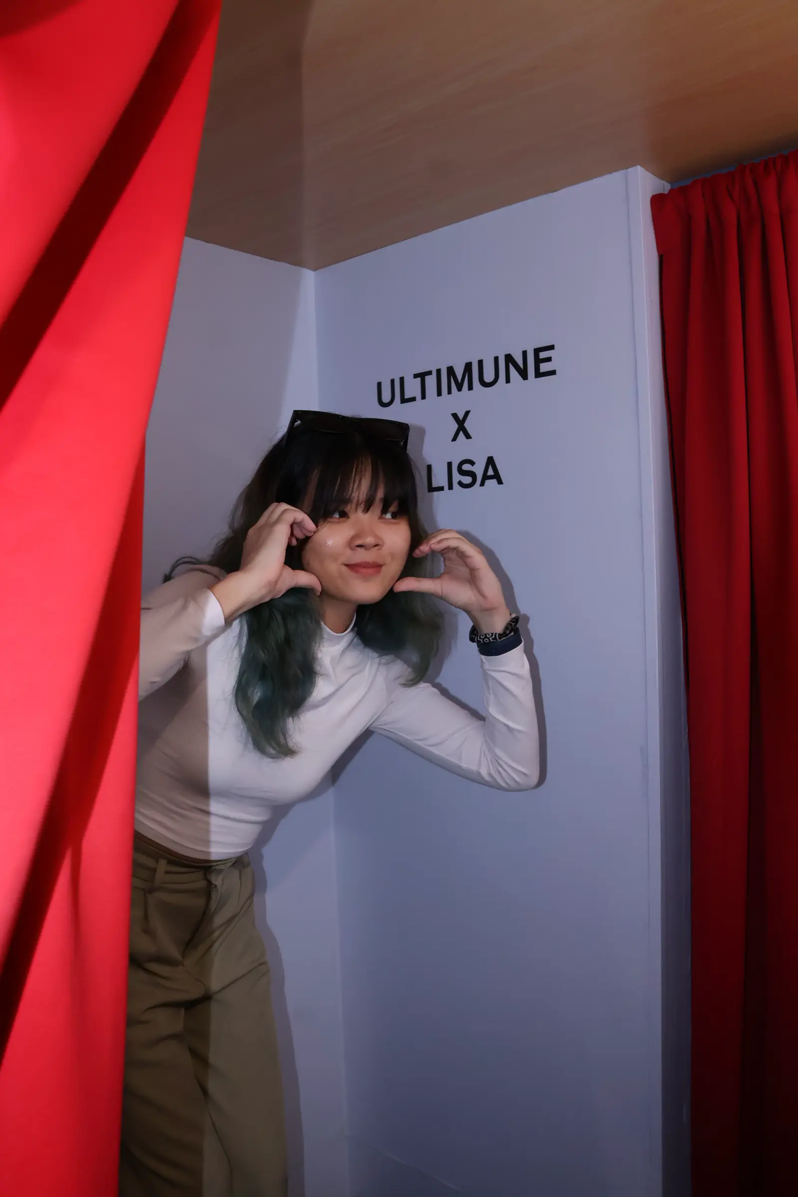 Young woman making finger hearts beneath the ULTIMUNE x LISA wall sign inside the Shiseido photo booth