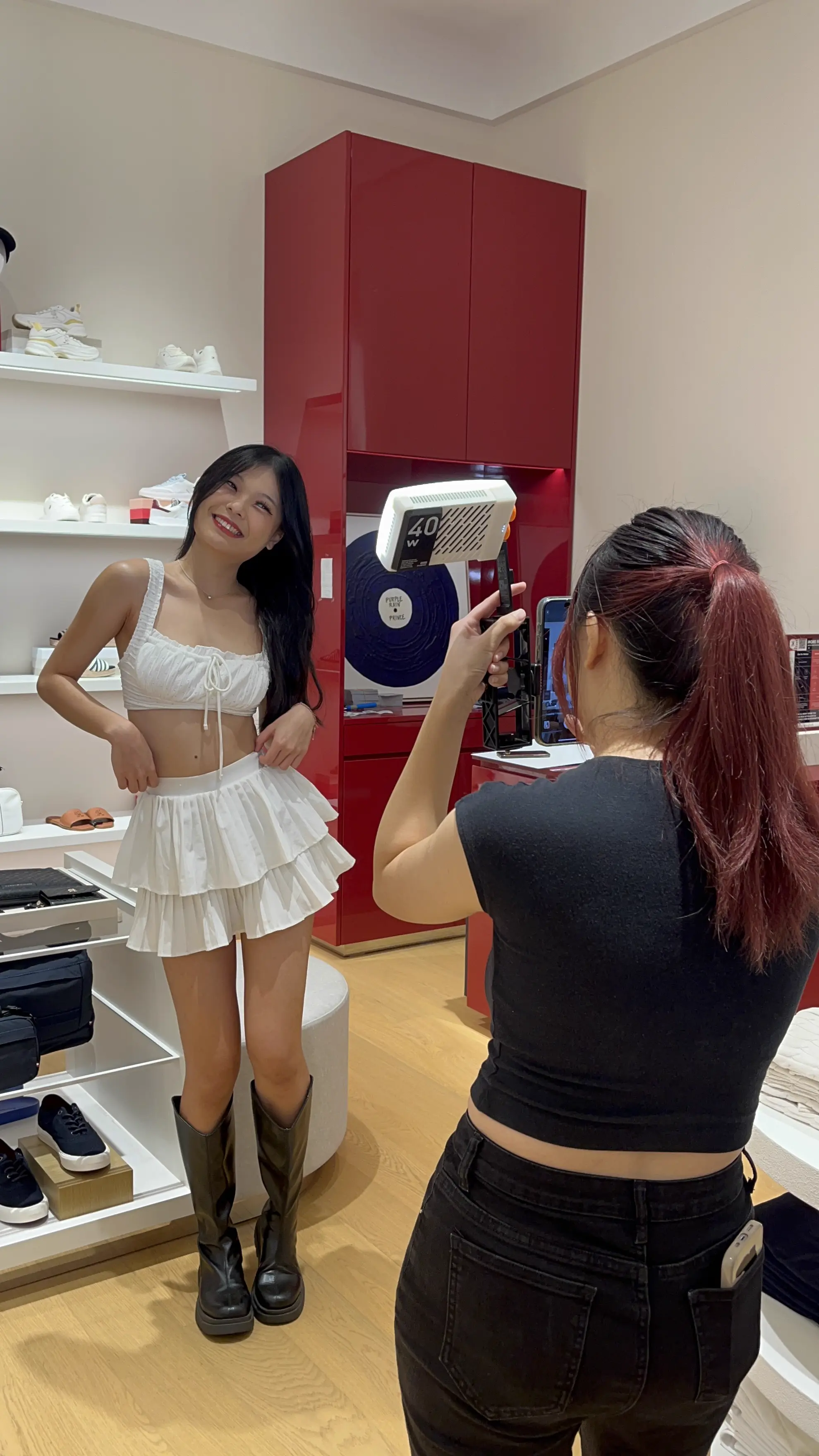 Photographer using a ring light to capture a woman posing in a white outfit and boots inside the Tommy Hilfiger store
