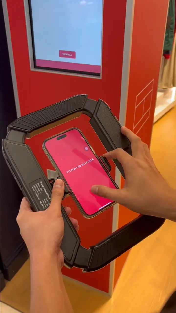 Hands placing a phone on the Tommy Hilfiger booth scanner showing the branded download screen