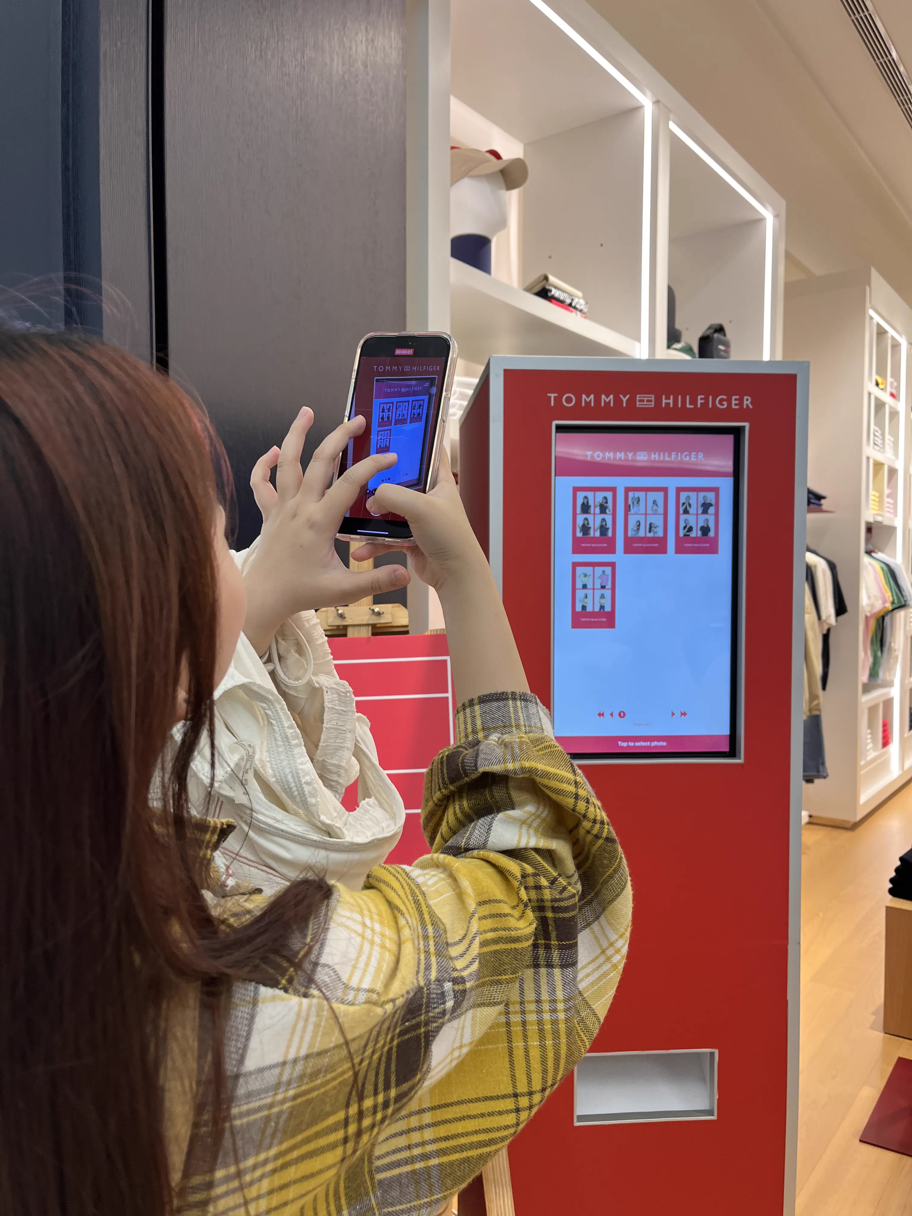 Visitor photographing the Tommy Hilfiger photo booth kiosk screen with her phone to download her photo strip